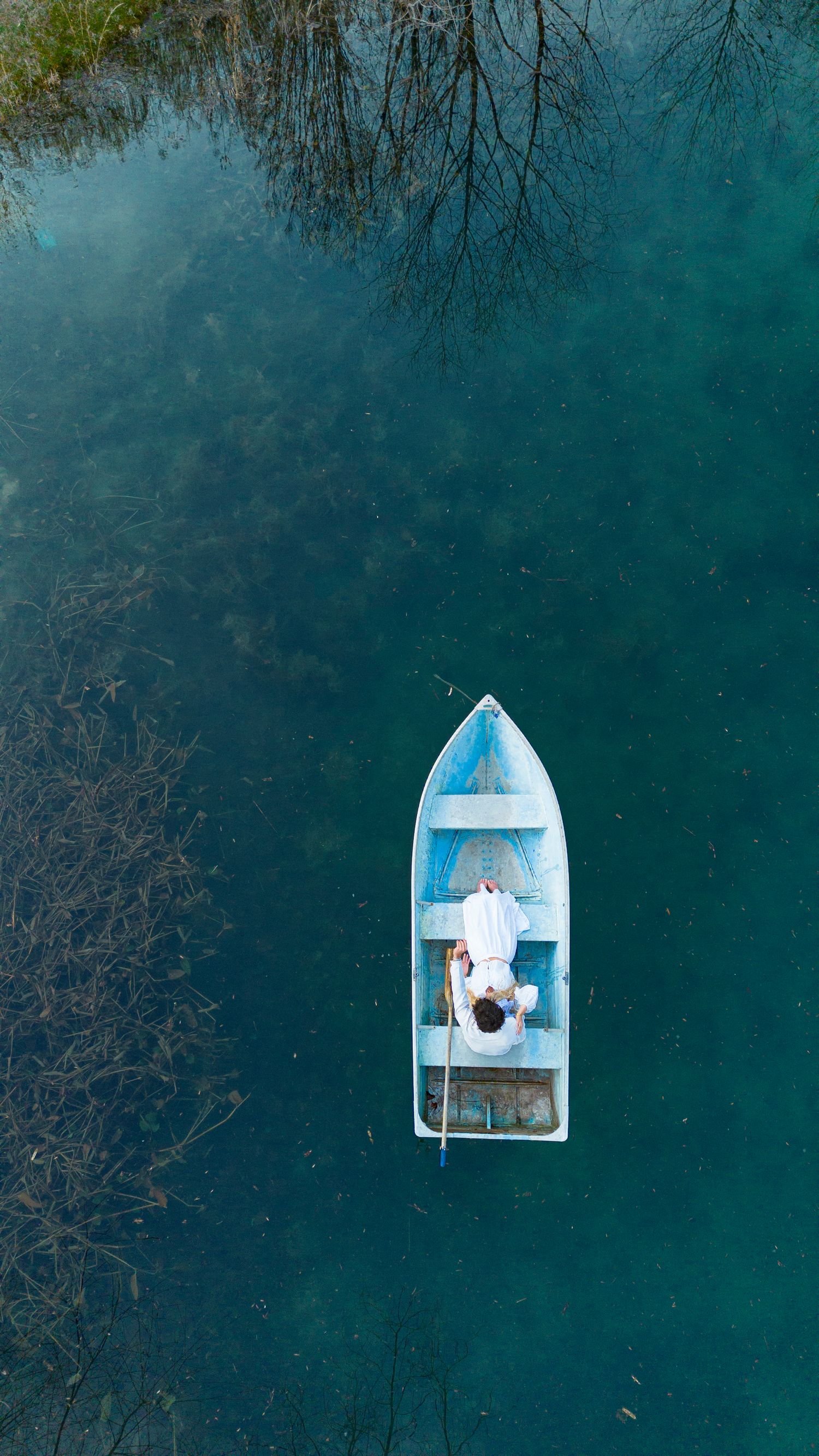 Aerial drone view of person relaxing in a small blue boat on clear turquoise water.