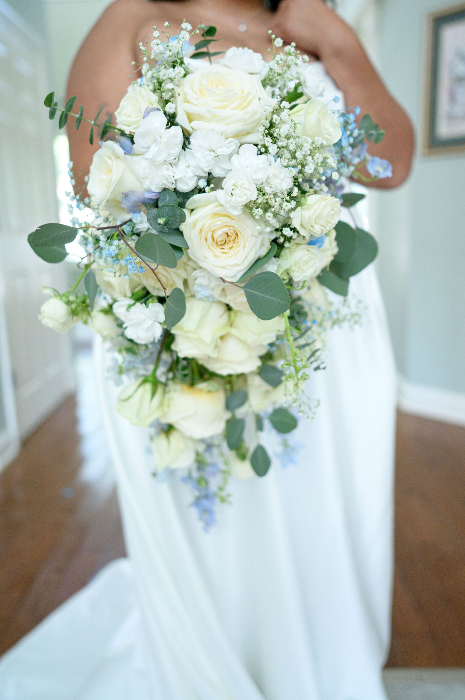 Bride holding a cascading wedding bouquet with white roses, baby's breath, eucalyptus, and blue delphinium flowers.