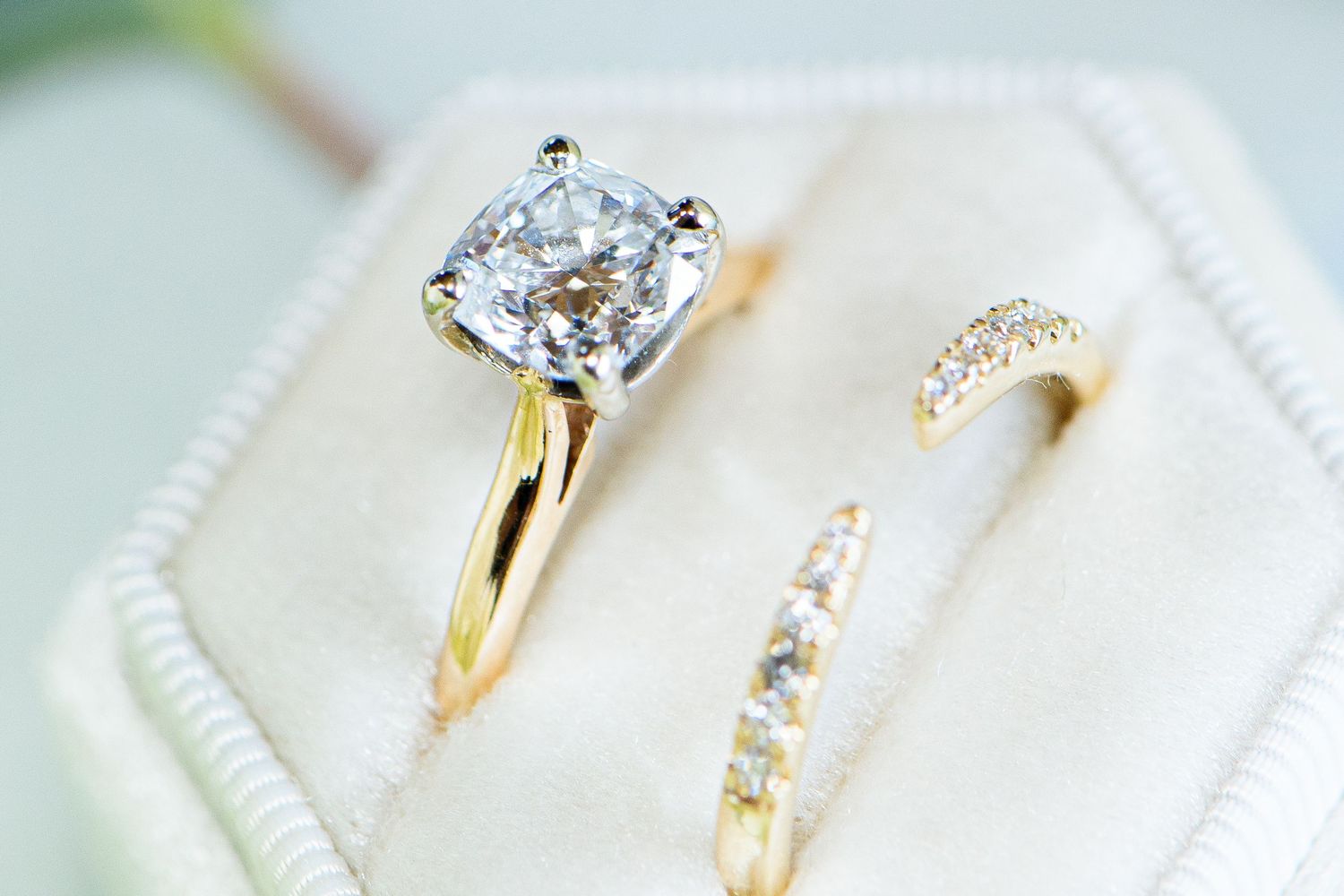 Gold solitaire diamond engagement ring paired with diamond band displayed in ivory velvet box.