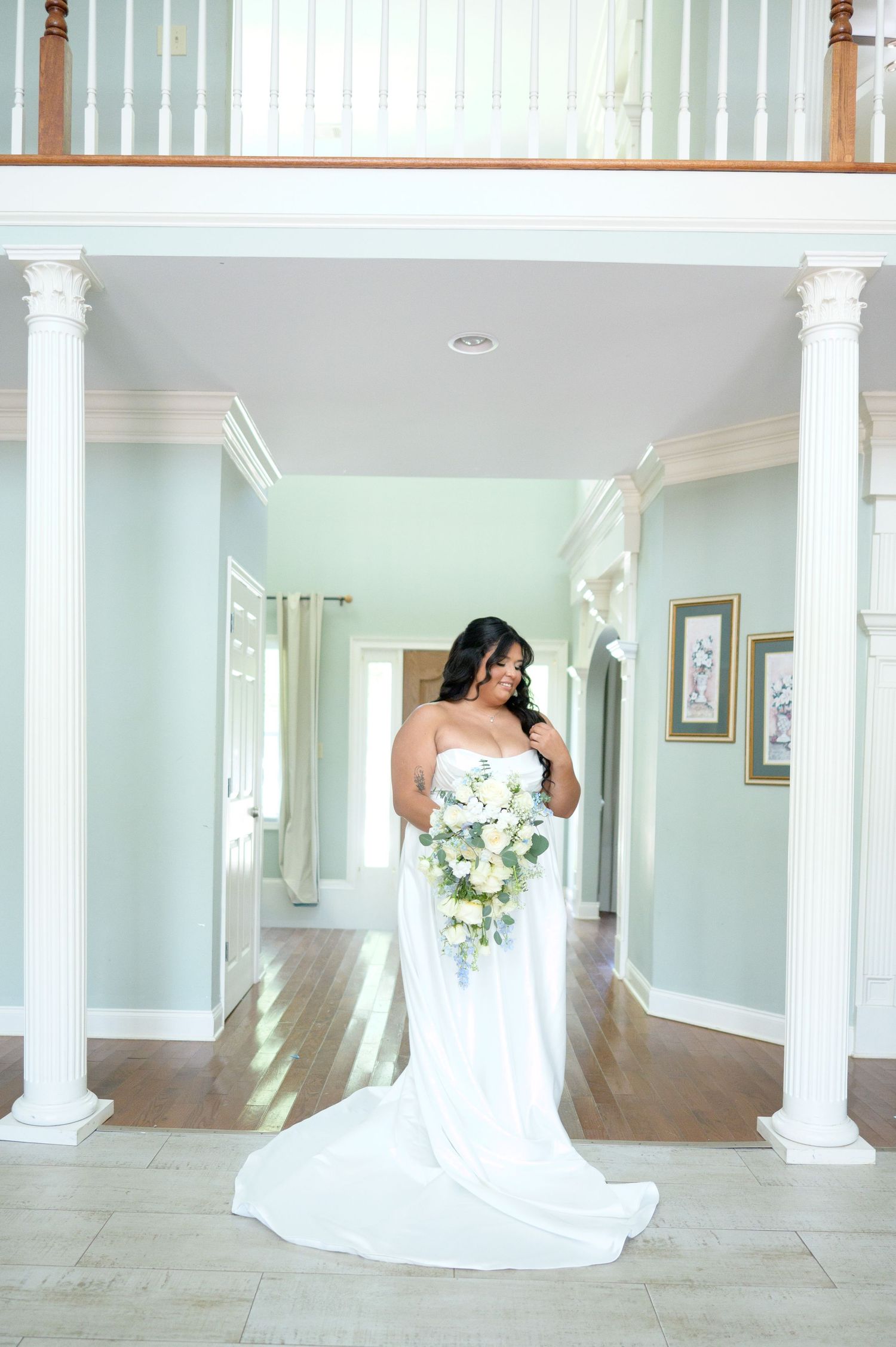 Bride in a strapless white gown holding a bouquet stands between elegant columns in a grand hallway.