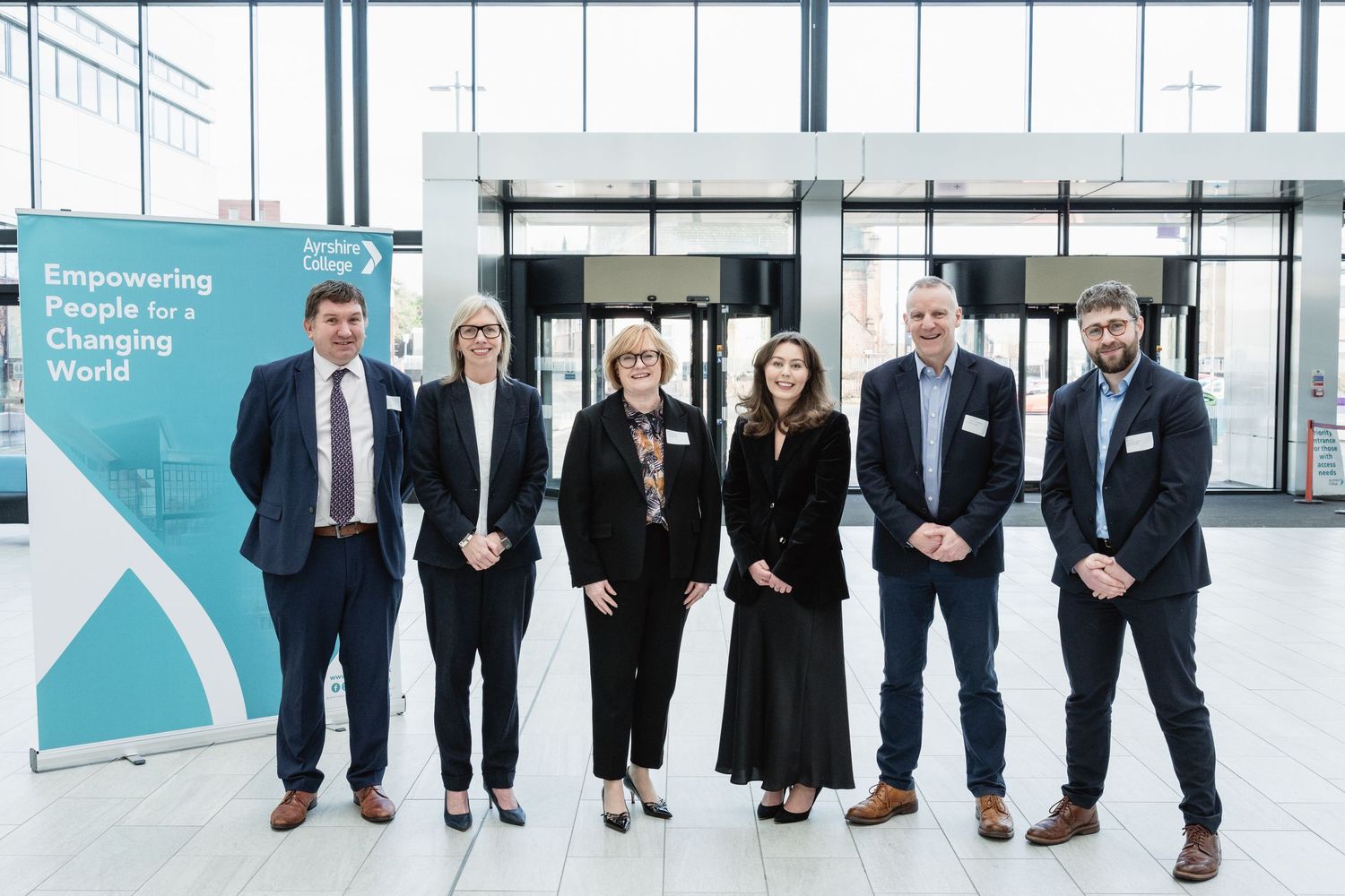 Seven professionals posing together in a modern conference venue beside an Empowering People for a Changing World banner.