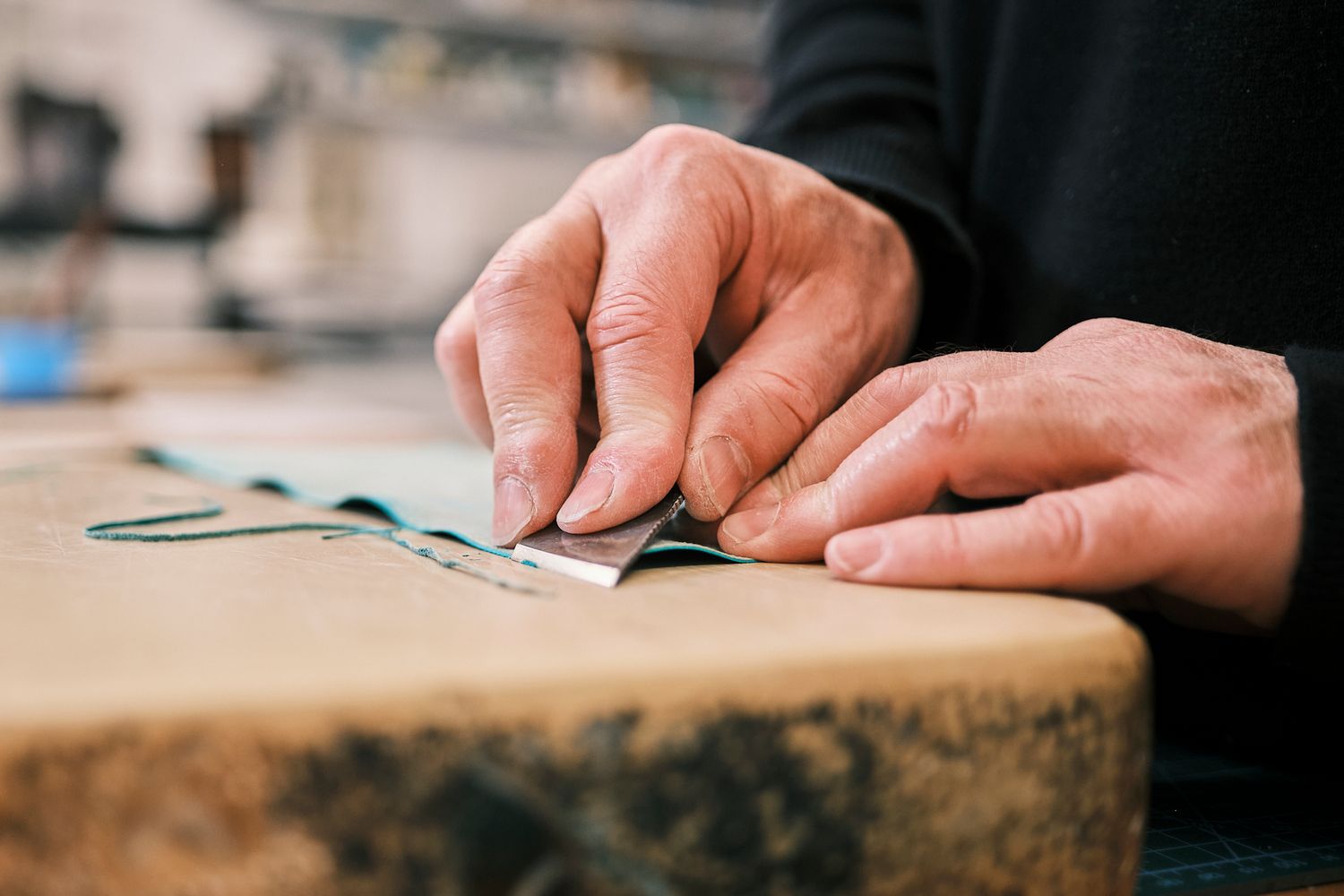 Close-up of hands carefully crafting leather on a wooden surface in a traditional artisan workshop.
