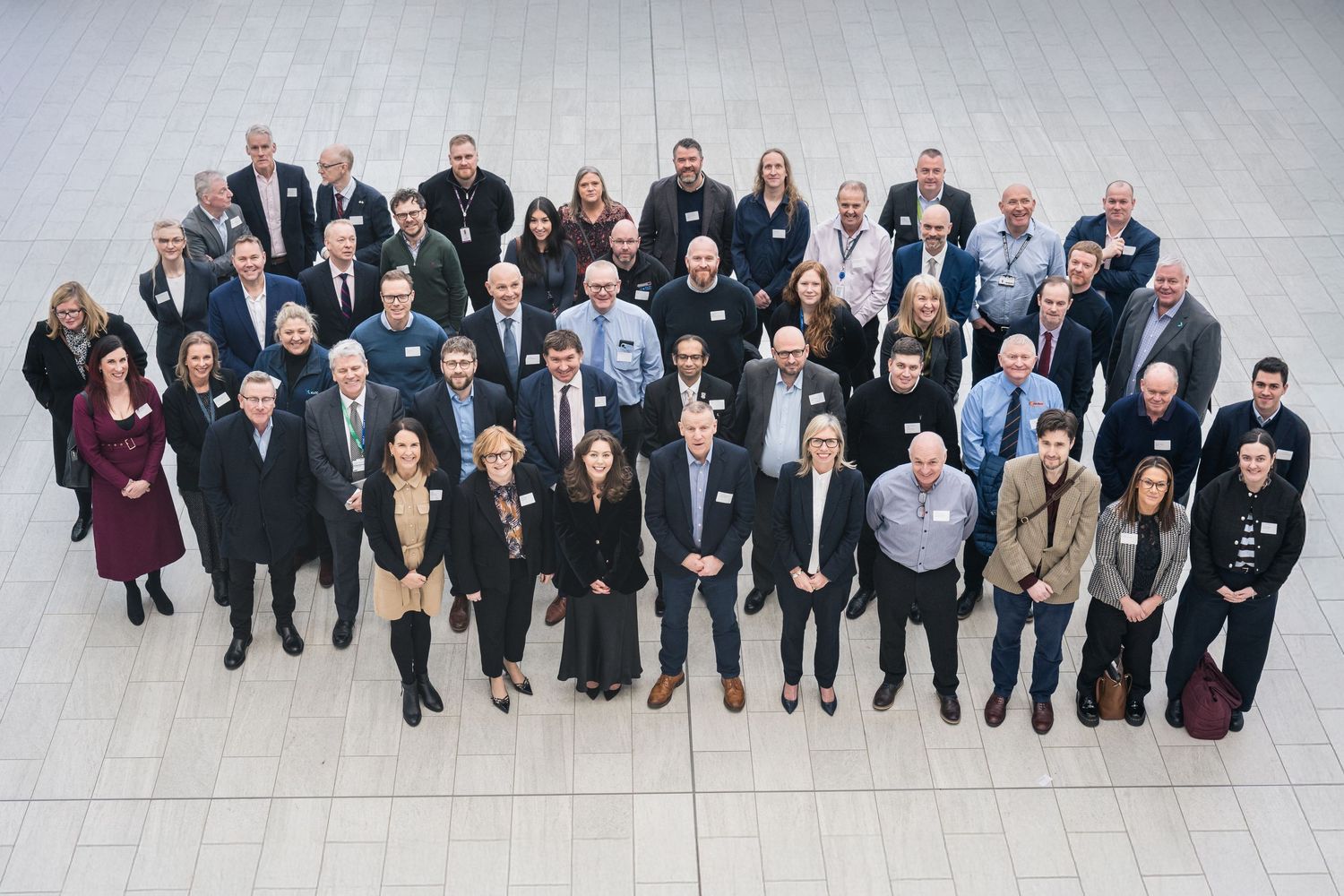 Large group of business professionals posing for a formal group photo in a modern atrium conference venue.