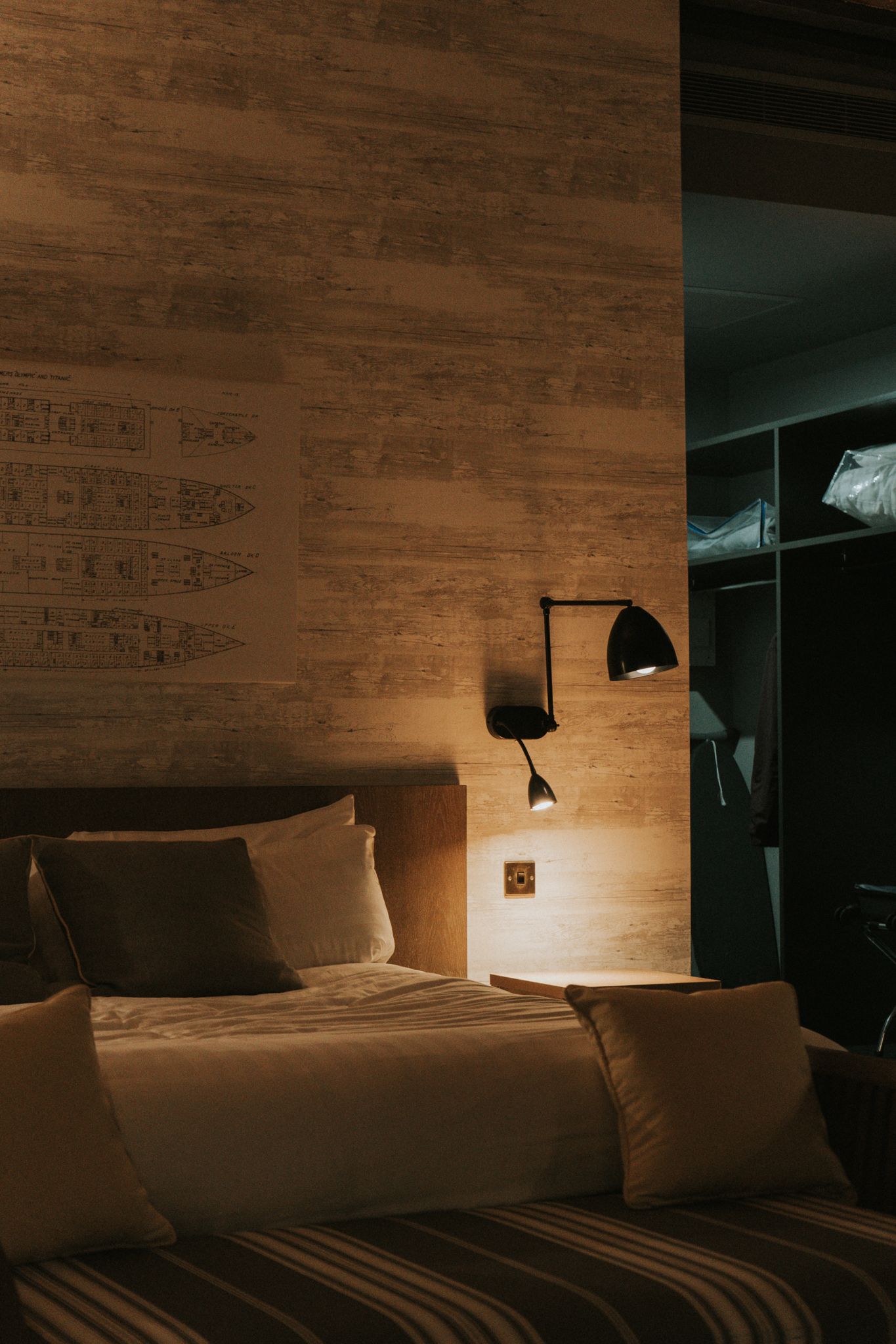 Warm hotel bedroom at night featuring textured wall panel, adjustable wall sconce, and pillows.