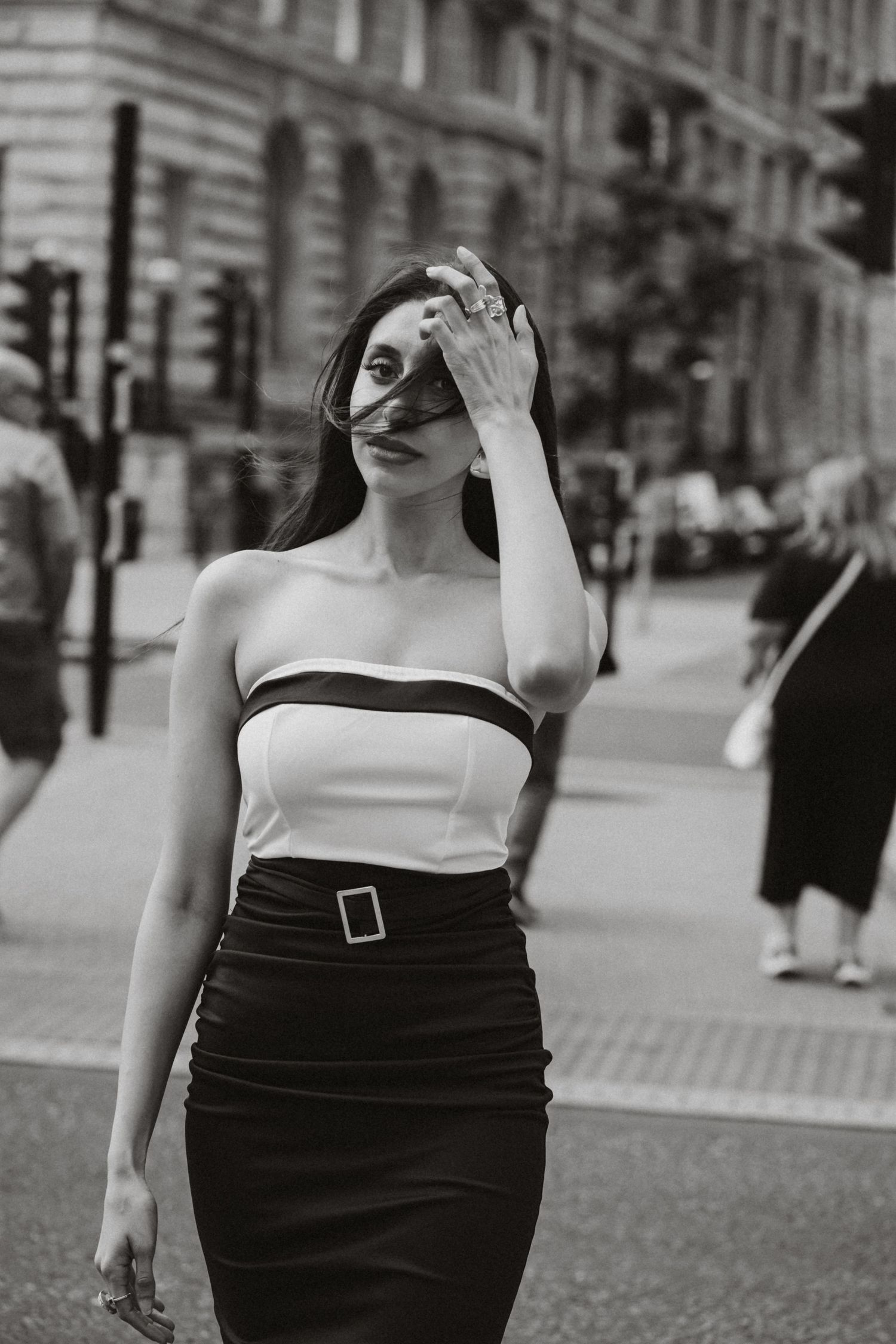Black and white street photo of a stylish woman in a strapless top and pencil skirt covering her face.