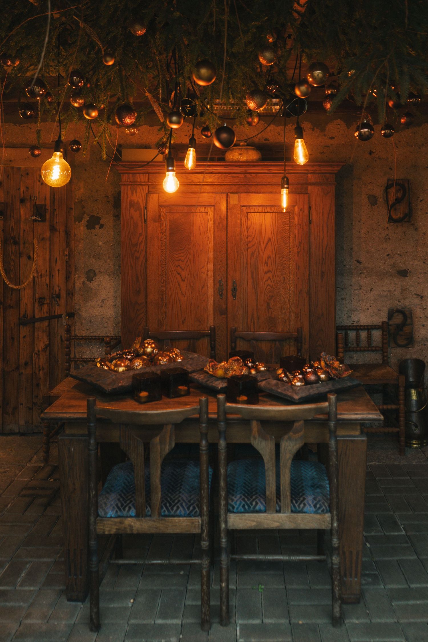Cozy dimly lit dining room with vintage wooden furniture, Edison bulb pendants, and decorative platters on a rustic table.