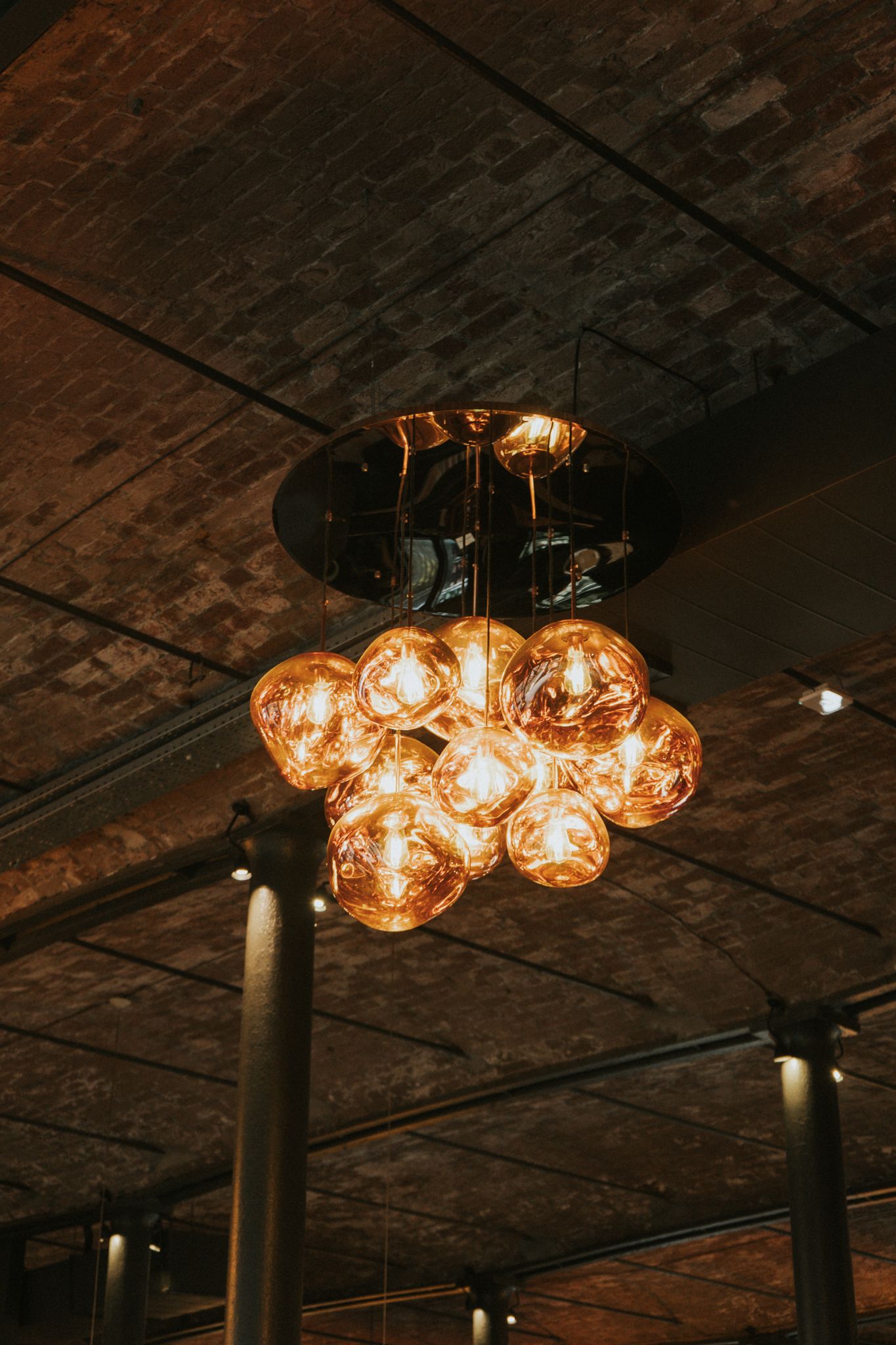 Cluster of amber globe pendant lights hanging from a dark exposed brick ceiling.