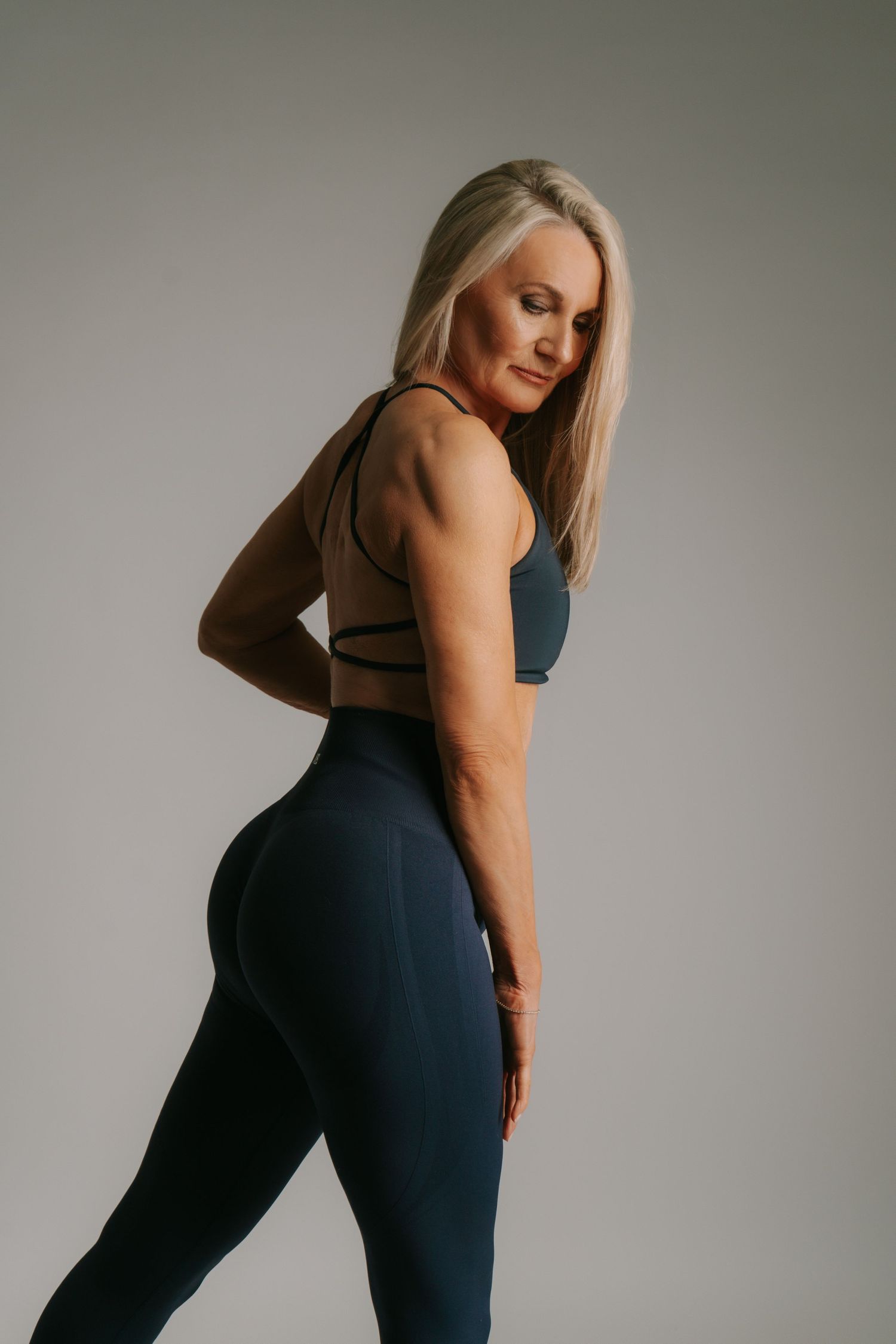 Fit blonde woman in navy blue sports bra and leggings posing in studio fitness photoshoot.