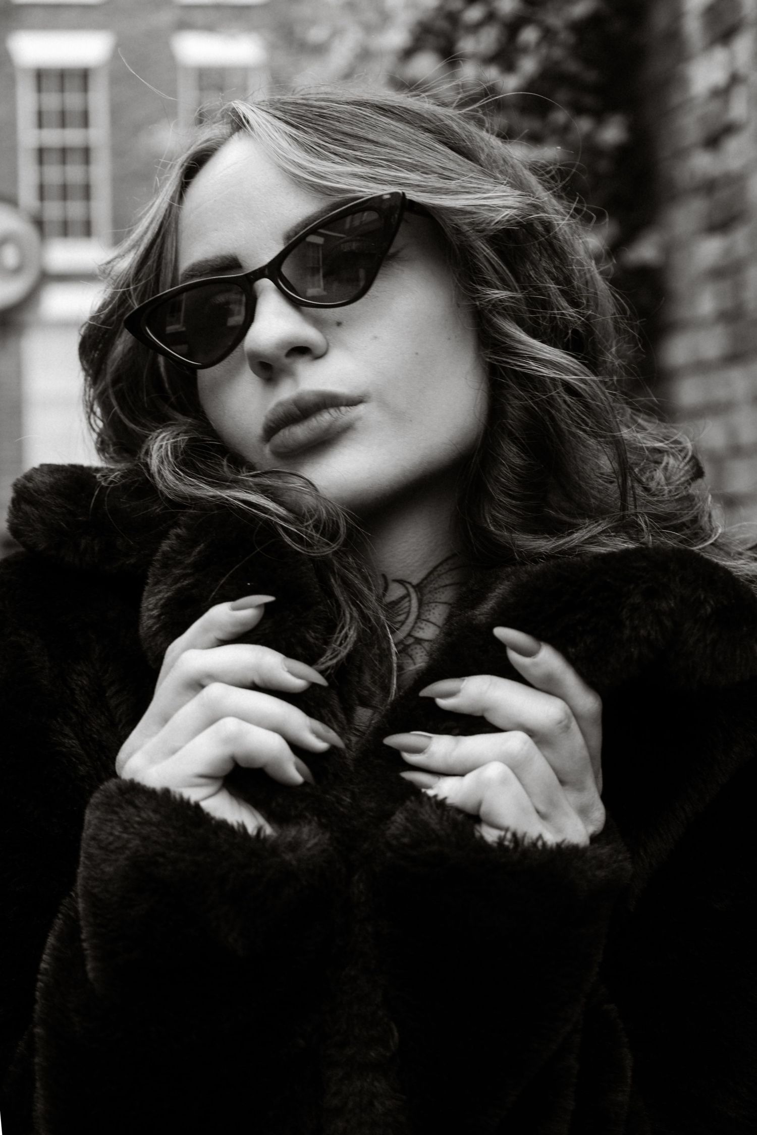Black and white portrait of woman in fur coat and cat-eye sunglasses outdoors.