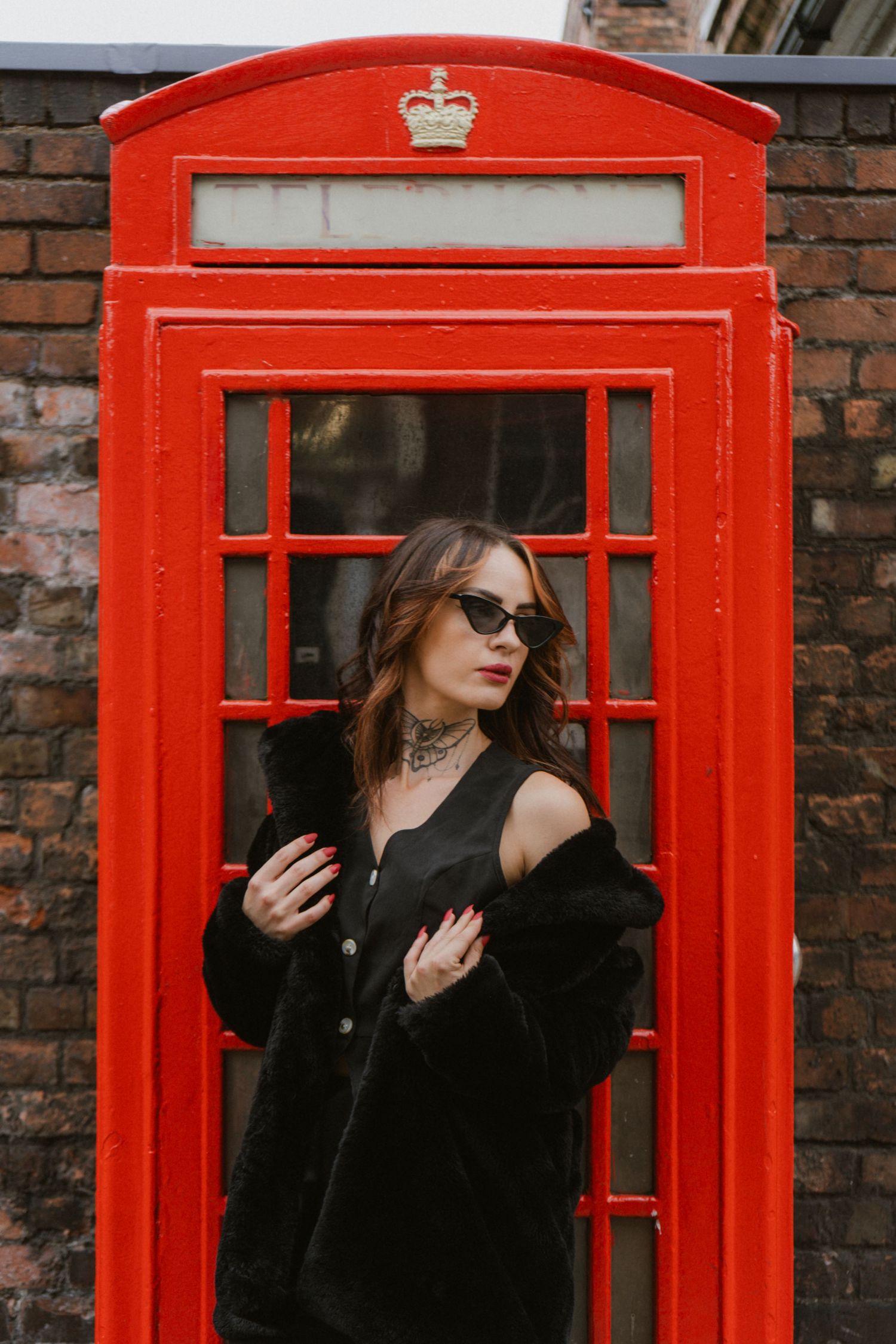 Stylish woman in black fur coat posing by iconic red British telephone box.