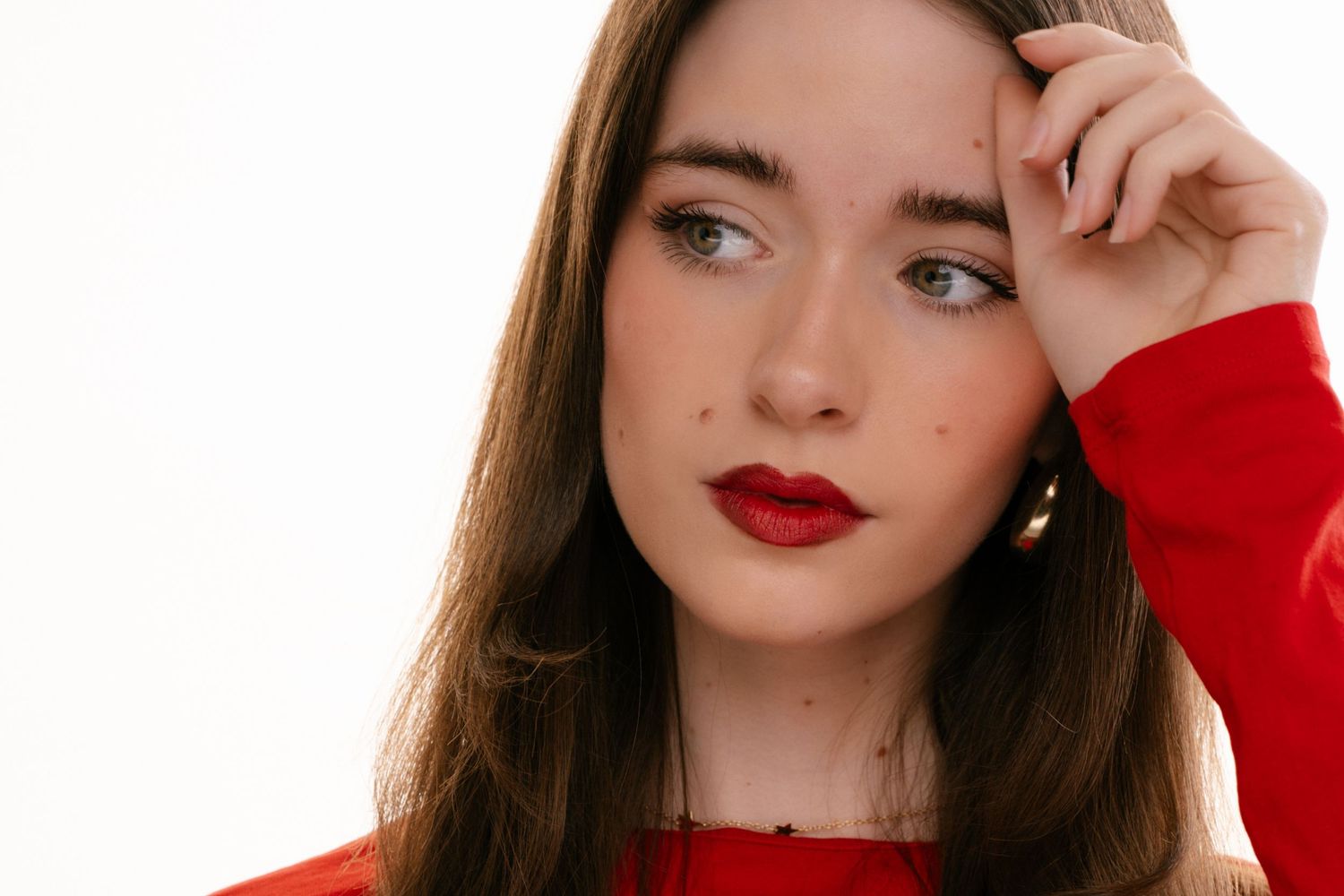 Young woman with red lips and freckles in red top poses against white background.