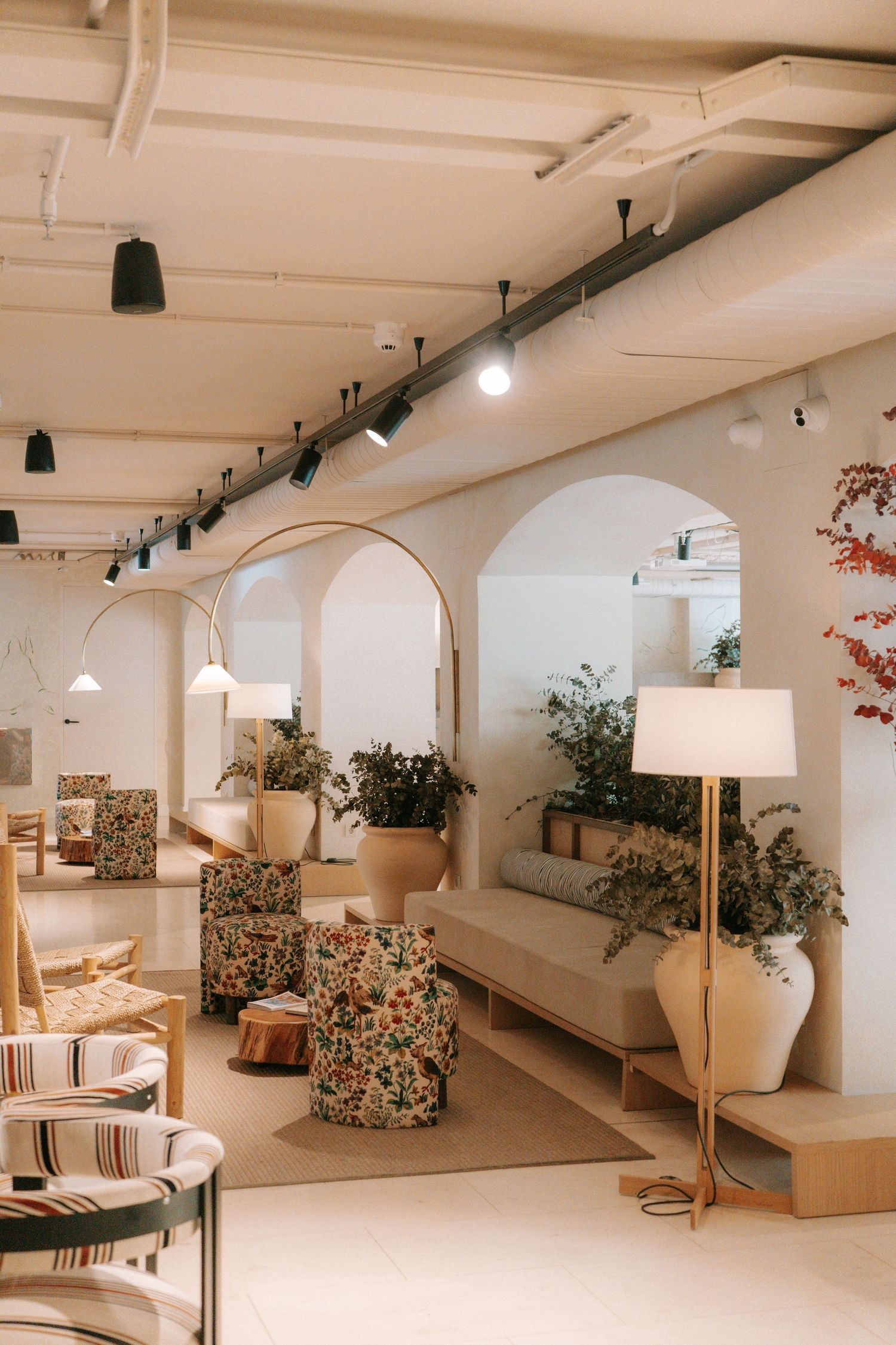Elegant hotel lobby featuring arched walls, floral seating, tall floor lamps, potted plants, and warm ambient lighting.