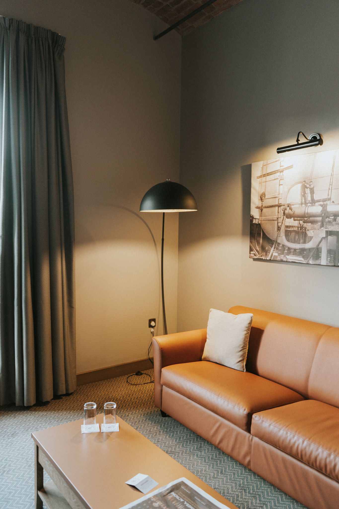 Cozy hotel suite sitting area with tan leather sofa, arc floor lamp, and industrial wall art.