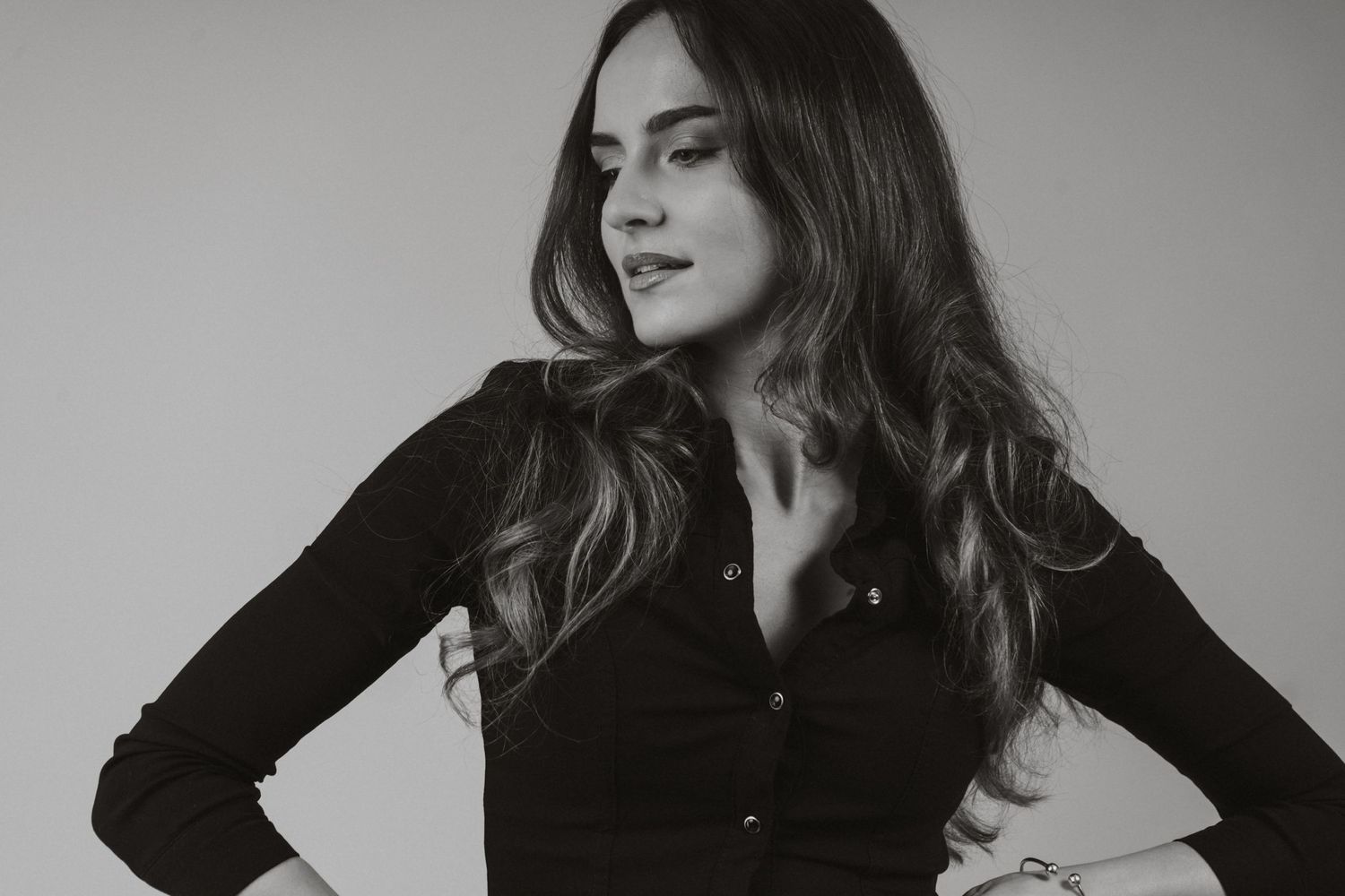 Black and white close-up of brunette woman in black button-up shirt with hands on hips.