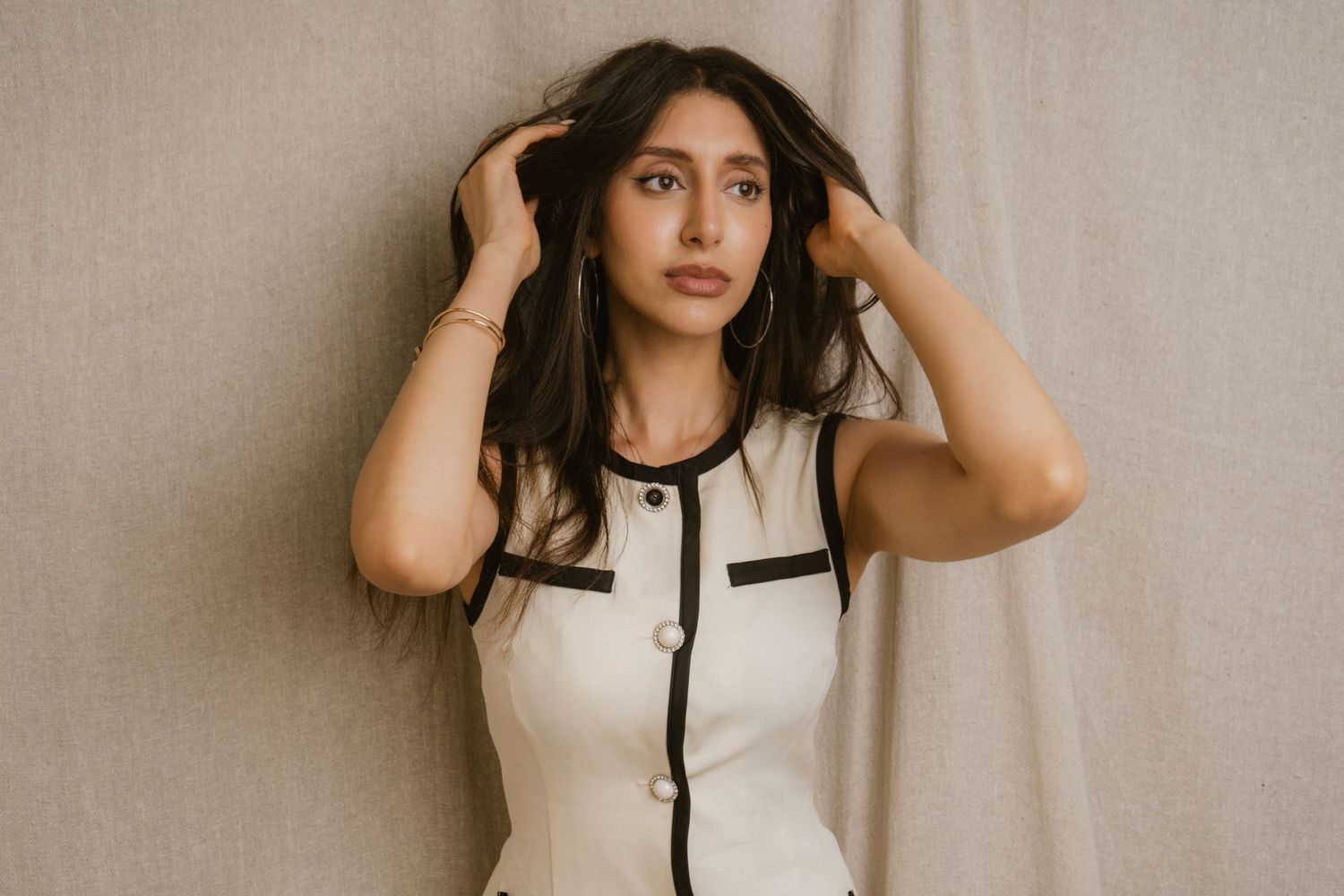 Young woman in white and black sleeveless dress posing with hands in hair.