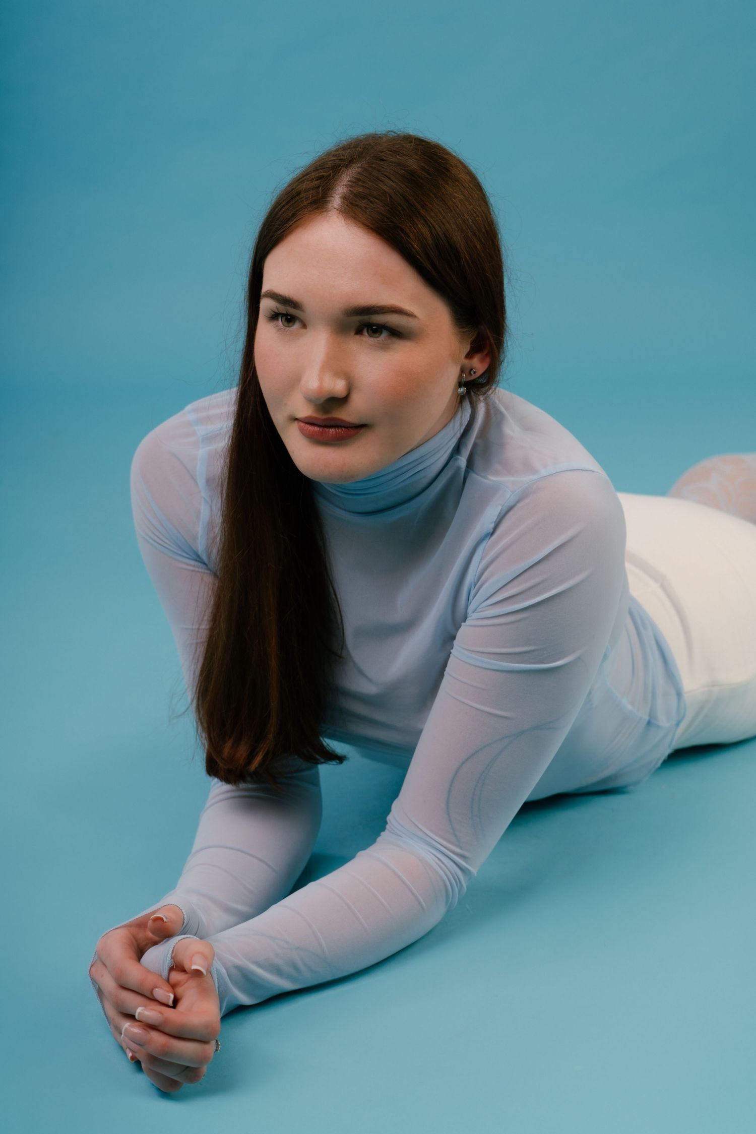 Young woman in blue mesh turtleneck lying on floor against solid blue studio background.