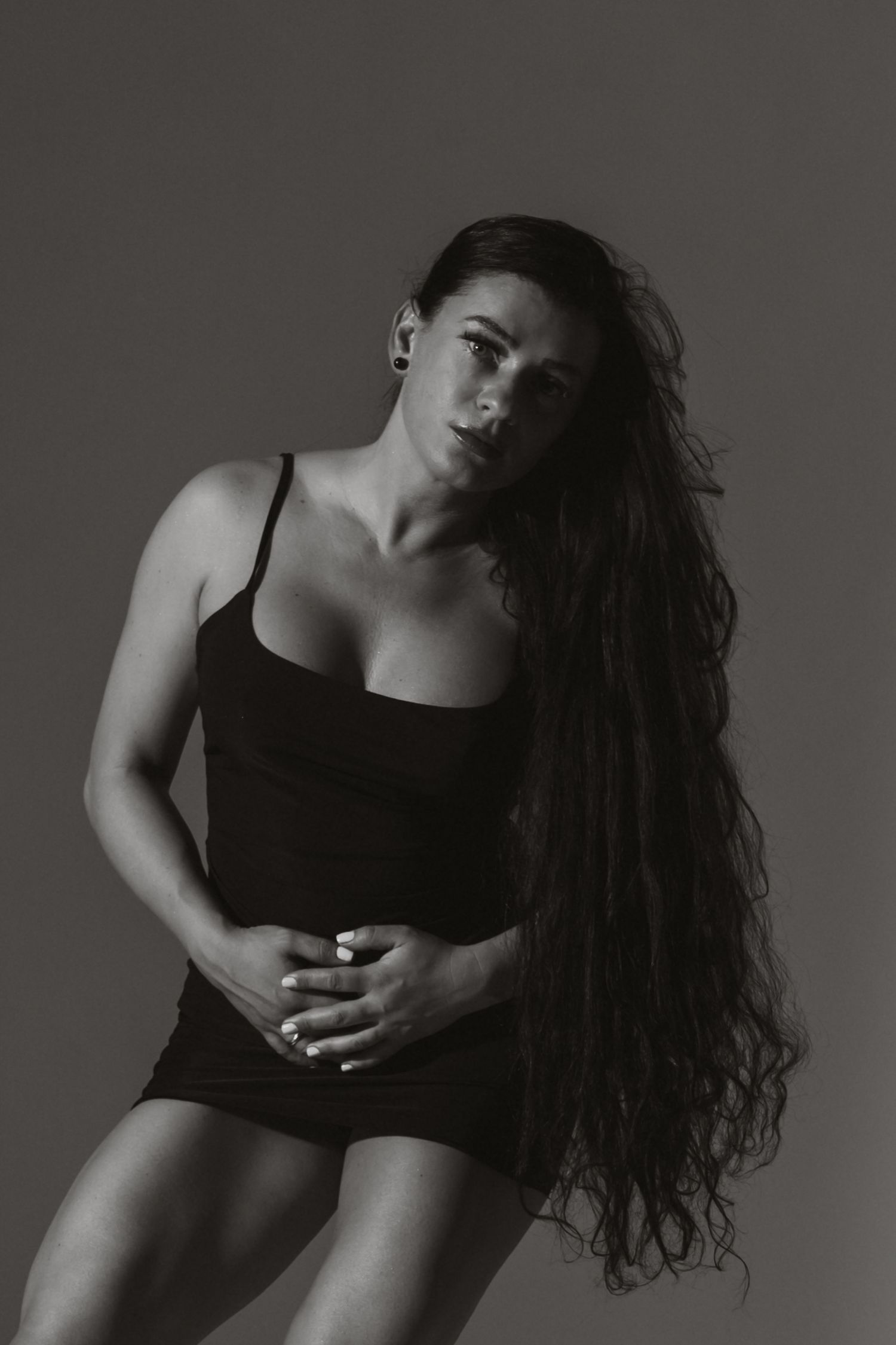 Black and white portrait of a woman with long wavy hair wearing a black mini dress in a dramatic pose.