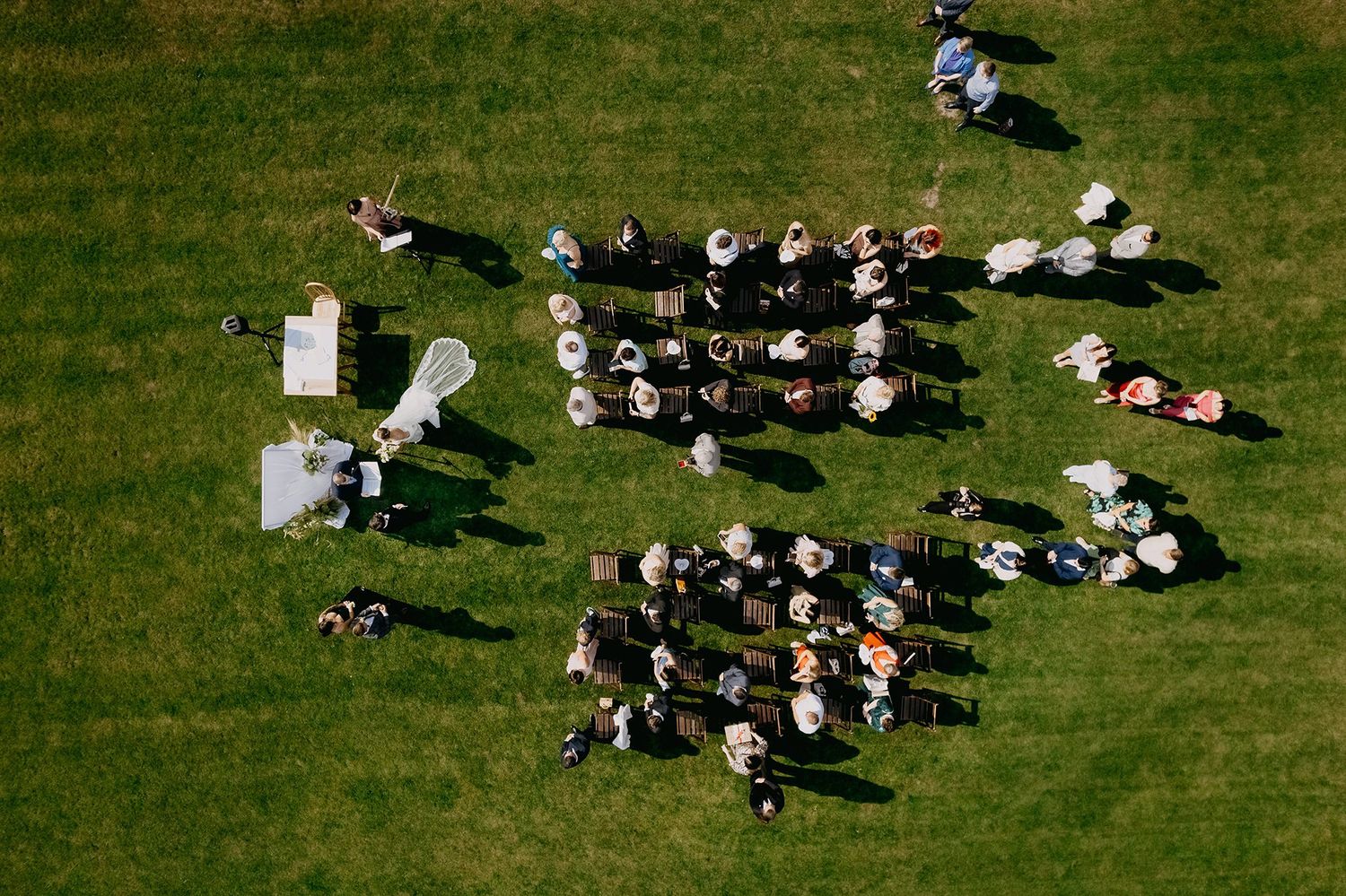 Aerial view of an outdoor wedding ceremony with guests seated in rows on a lush green lawn.