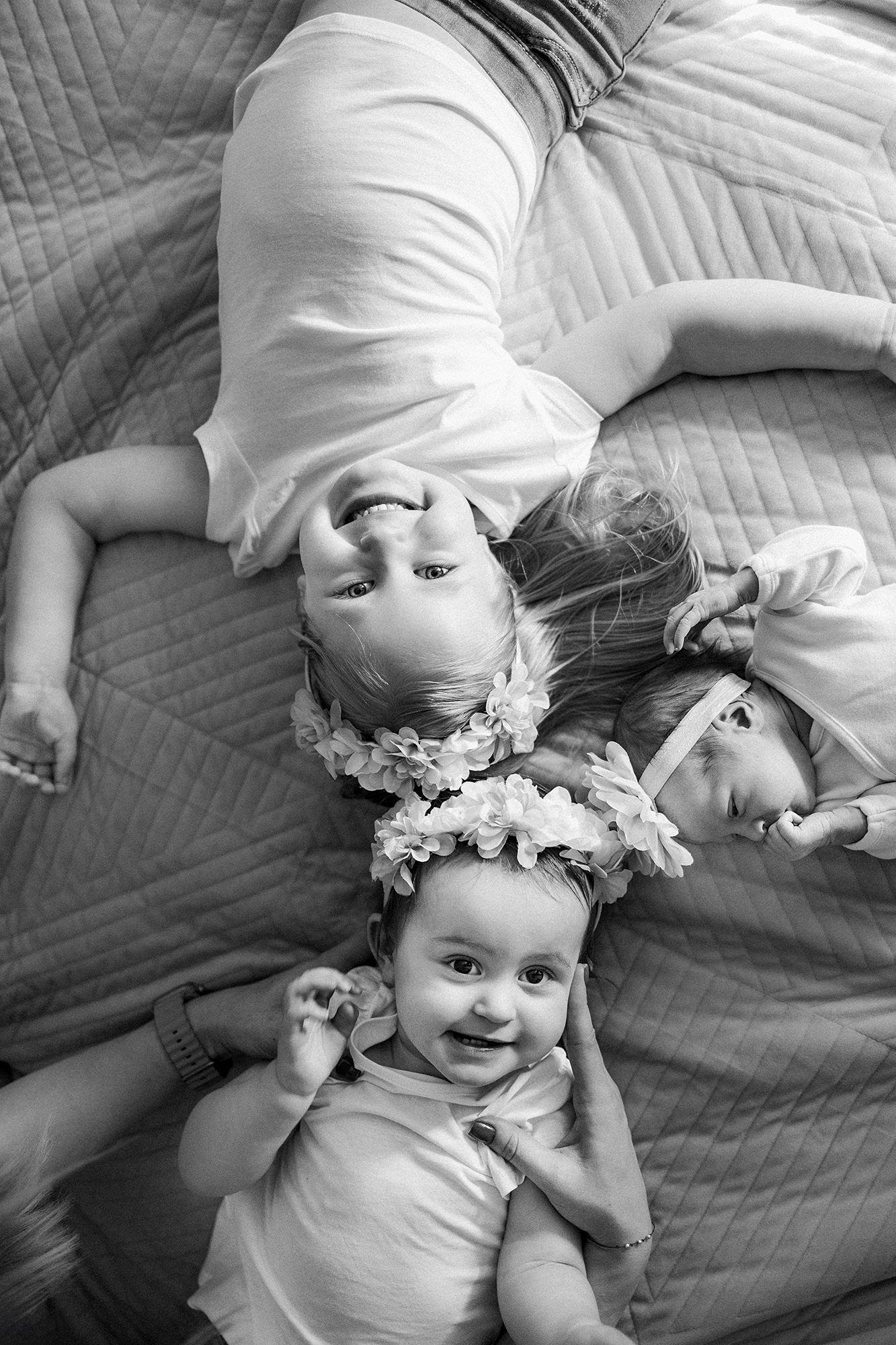 Black and white photo of three young children lying on bed wearing floral headbands.