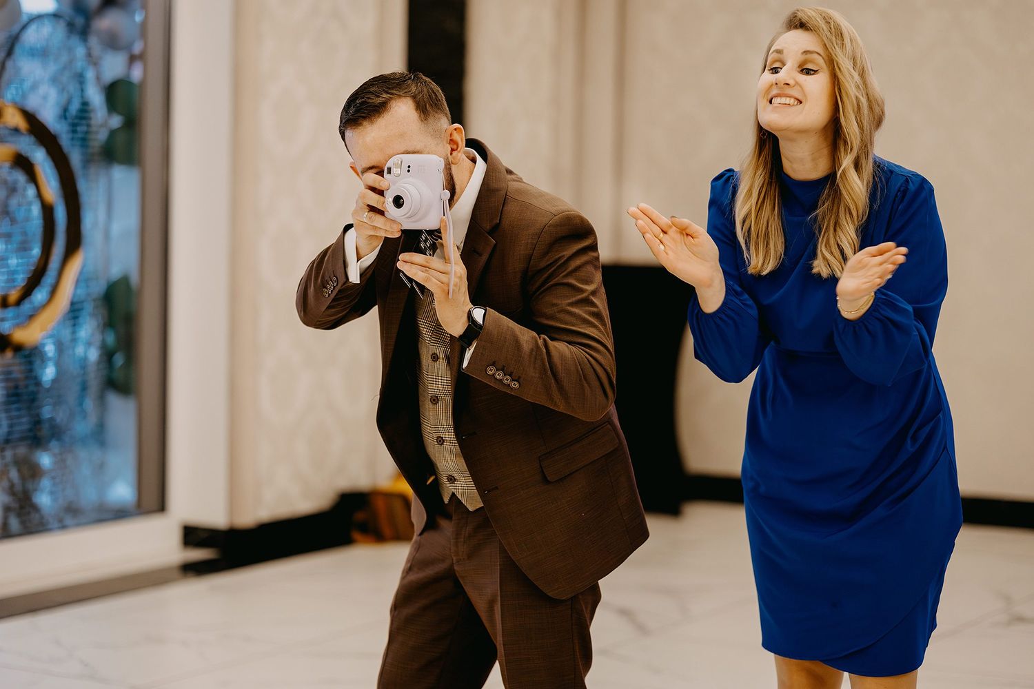 Man photographing with a tablet while a woman in a blue dress claps at a celebration event.