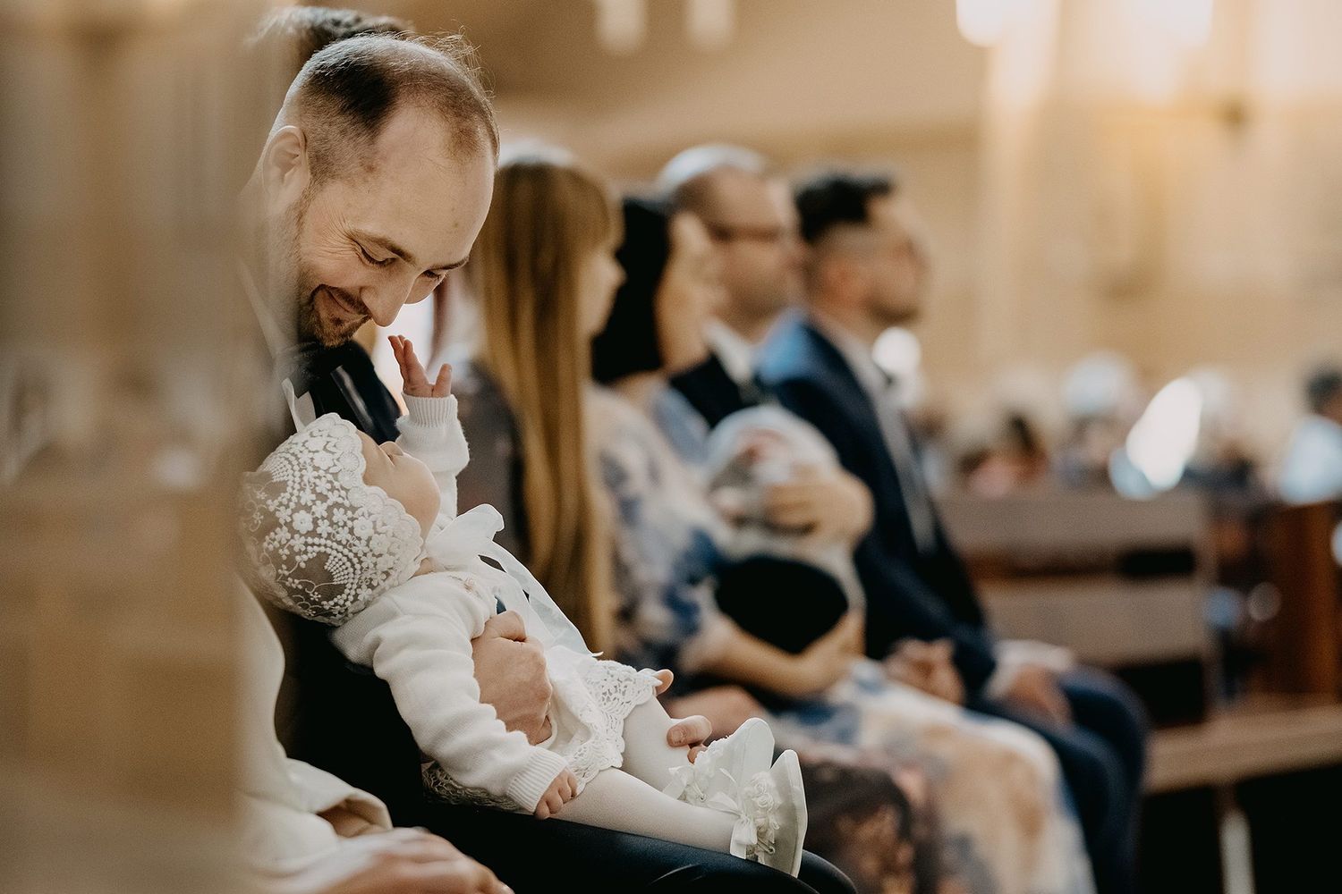 A father tenderly holds his baby in a lace christening gown during a baptism ceremony in church.