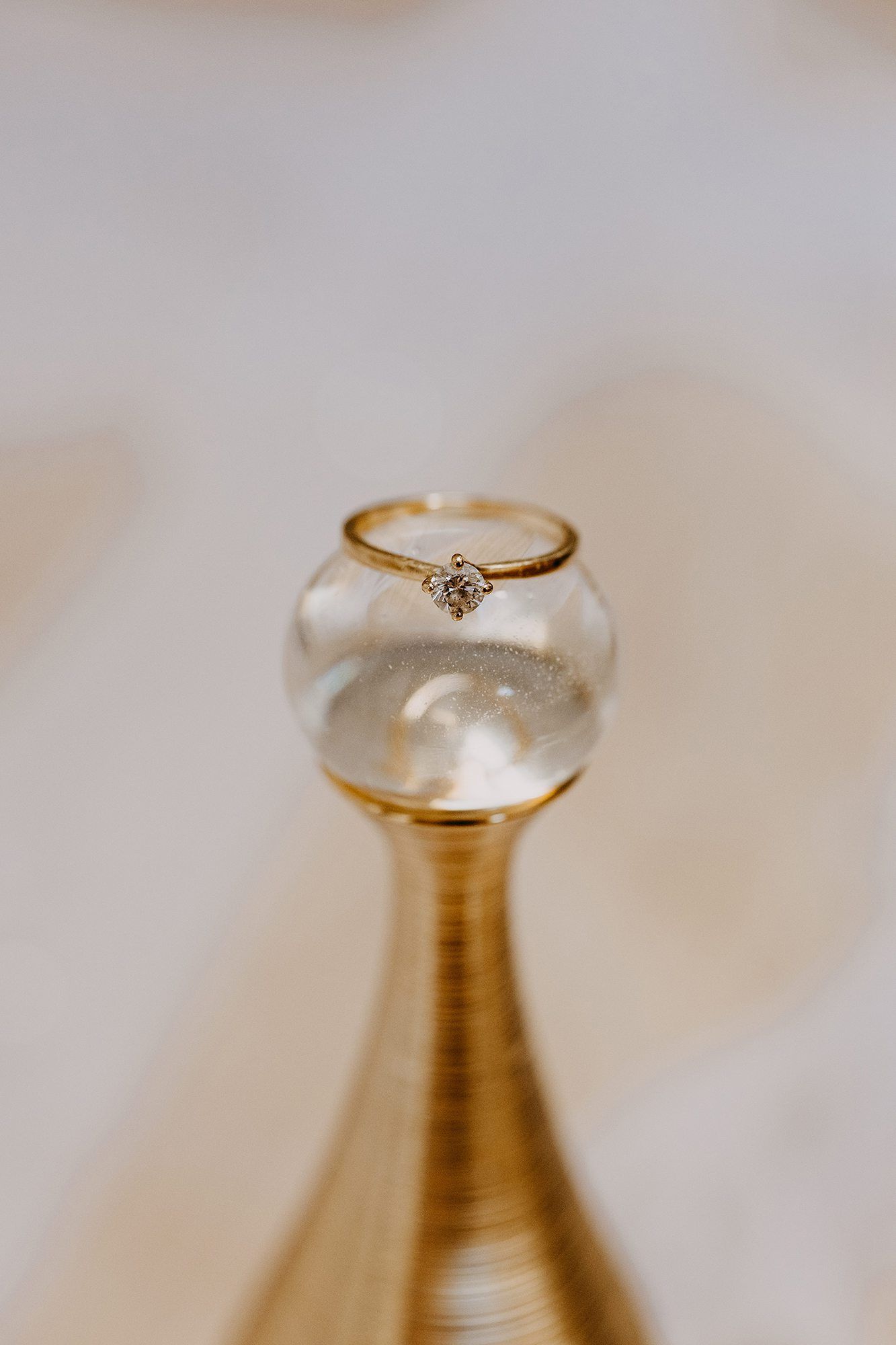 Close-up of a delicate diamond solitaire engagement ring resting on a gold decorative vase.