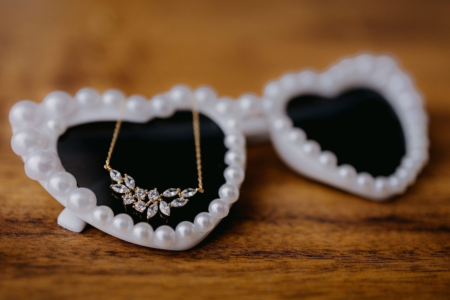 Pearl heart-shaped sunglasses with delicate gold leaf crystal necklace on wooden surface wedding accessories.