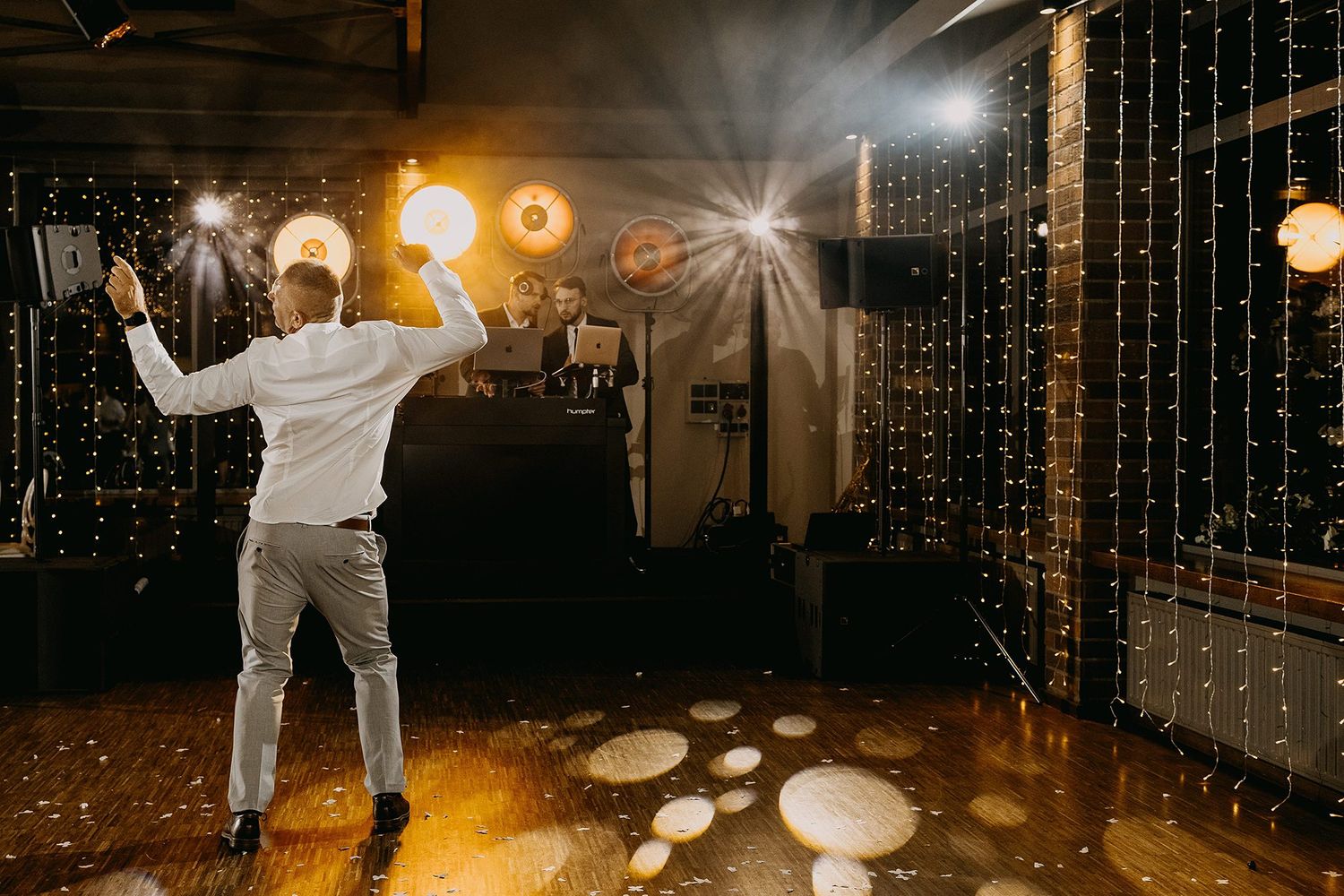 Guest dancing energetically on wedding reception dance floor with glowing string lights backdrop.