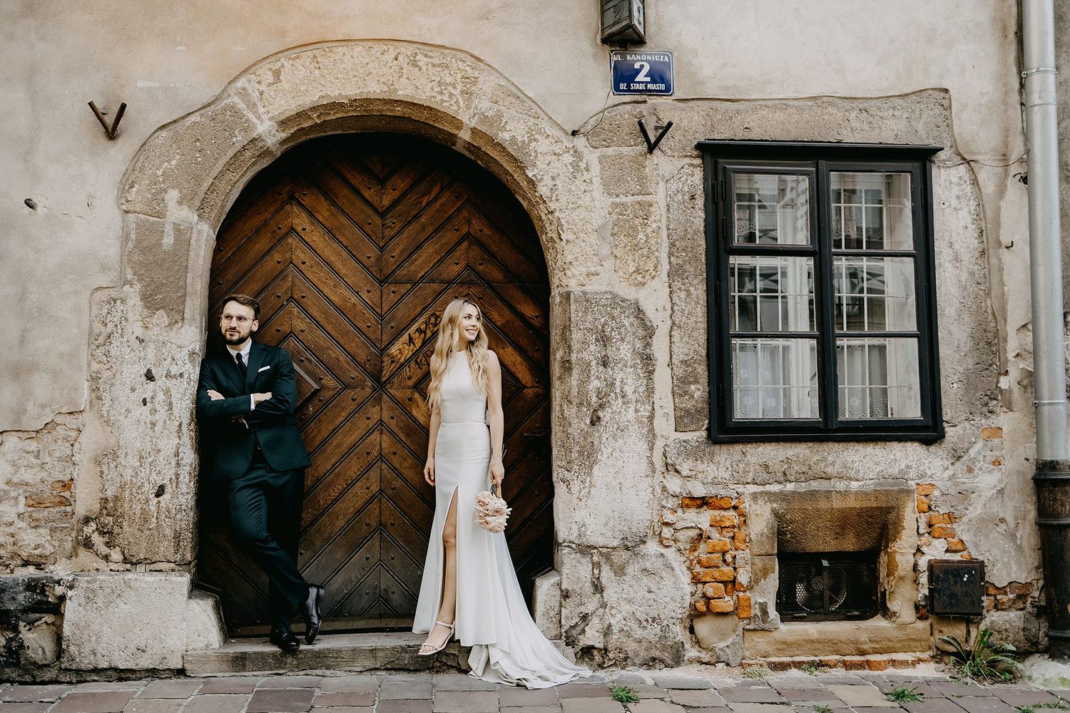 Wedding couple posing before rustic wooden door of historic stone building.