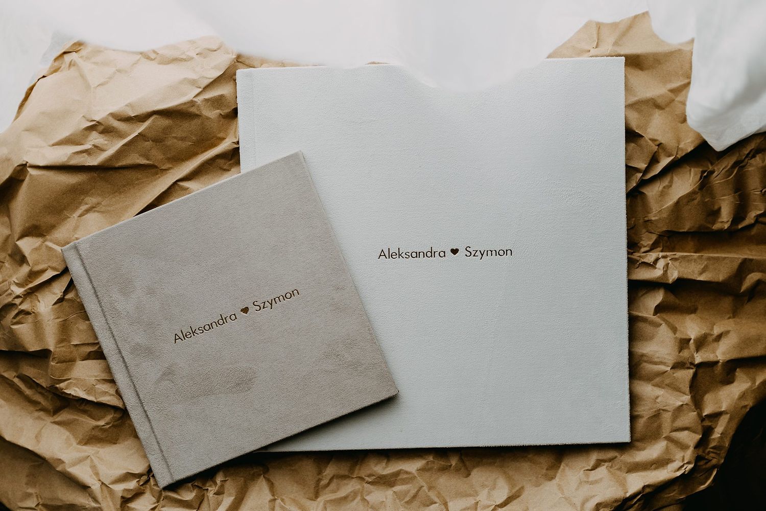 Matching linen-covered wedding photo album set with minimalist text on crumpled kraft paper.