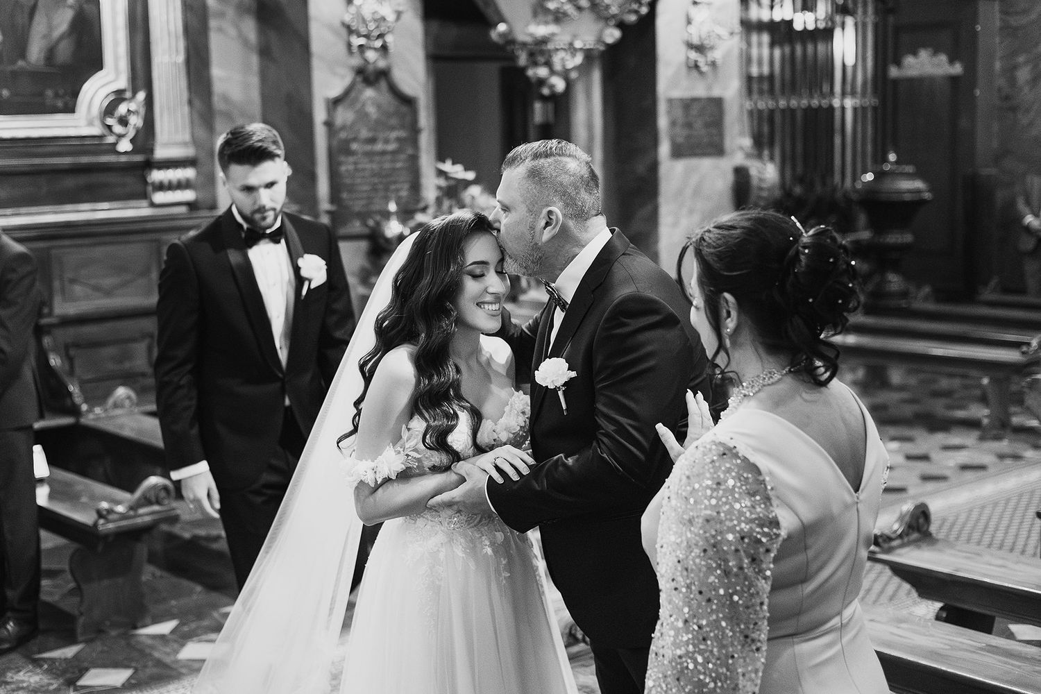 Groom kissing bride on cheek during emotional wedding ceremony in ornate church interior.