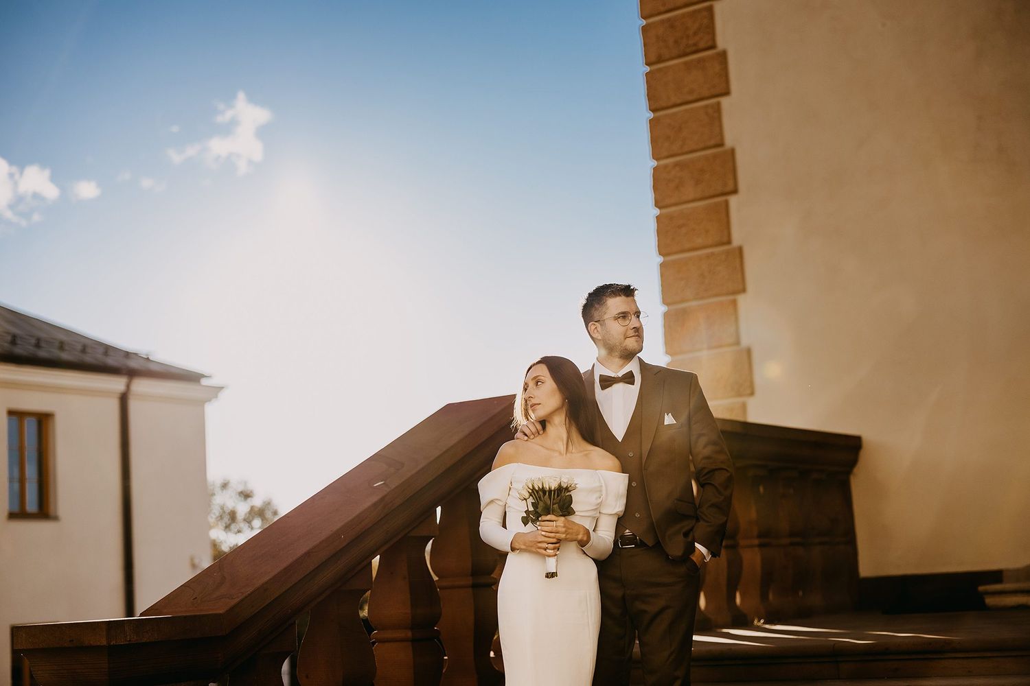 Bride and groom posing together on stone steps under a blue sky.