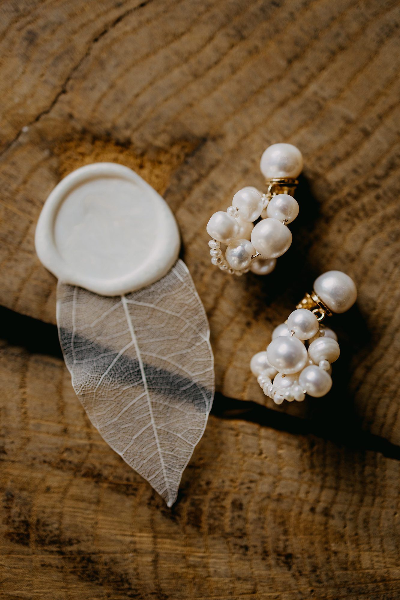 Pearl cluster earrings displayed on a rustic wooden surface with a wax seal and skeletal leaf.