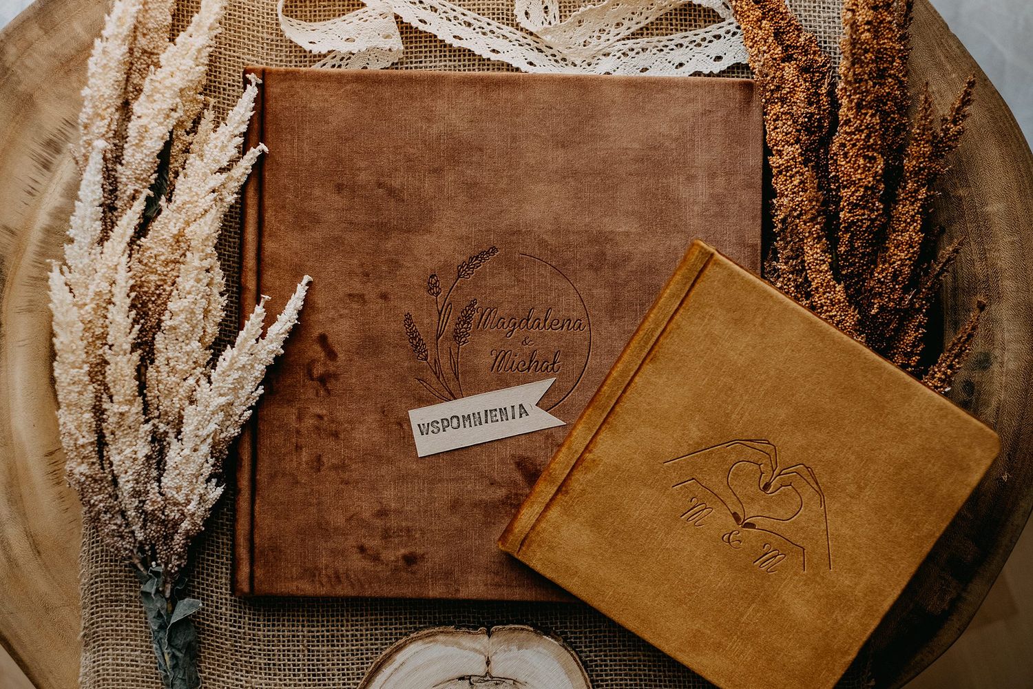 Two leather-bound photo albums on rustic wood surface surrounded by dried pampas grass.