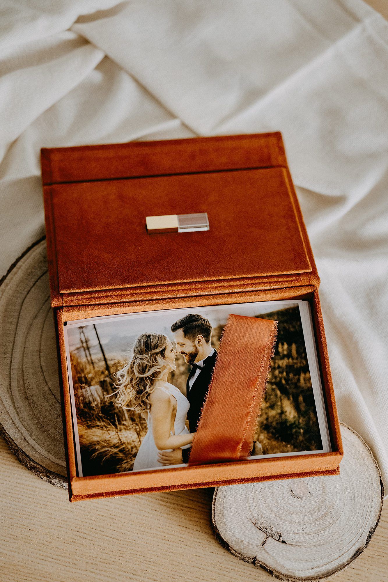 Brown leather wedding photo box open displaying couple portrait prints with ribbon.