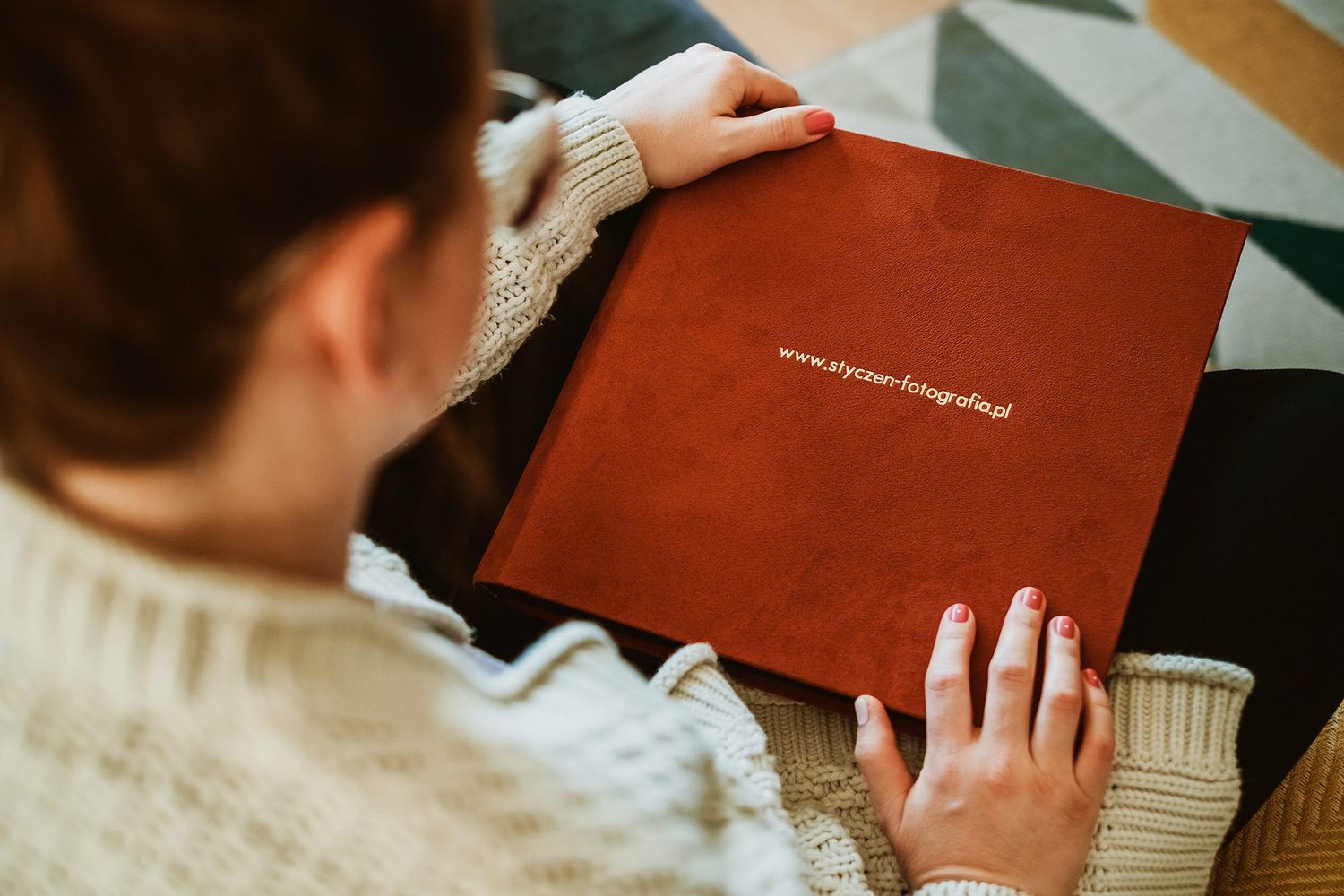 Woman in cozy sweater holding a red leather photography portfolio book with gold text.