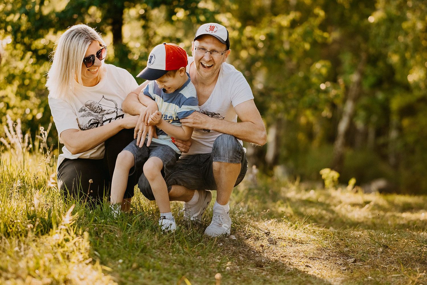 A happy family with a young boy laughs together outdoors in a sunny green park.