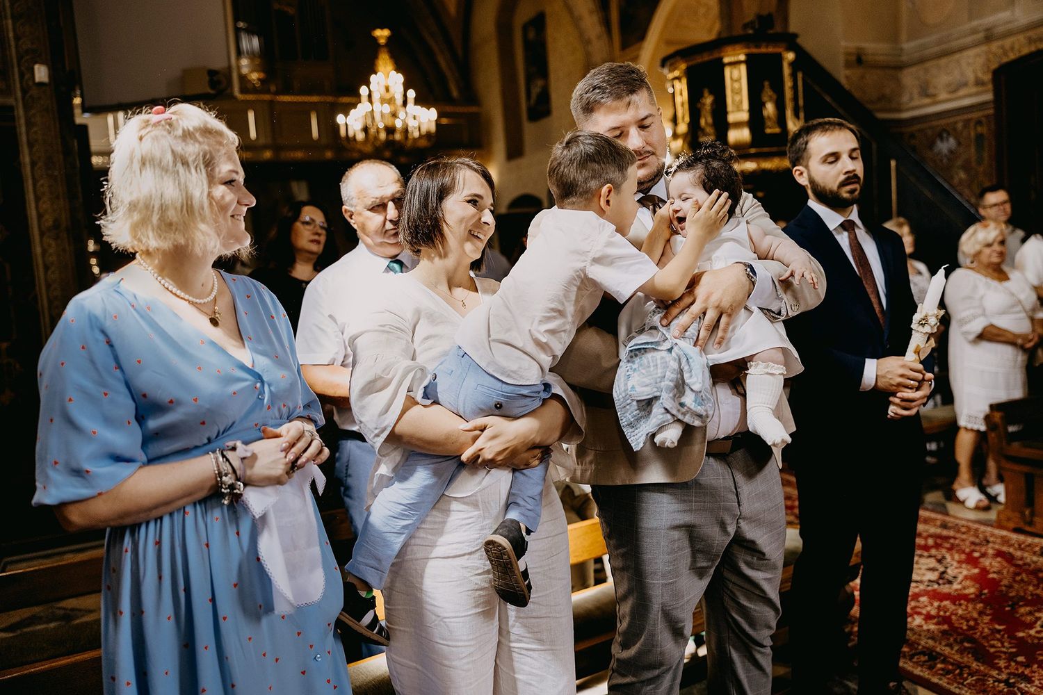 A joyful family gathers in a church after a baptism ceremony, sharing hugs and smiles in formal attire.