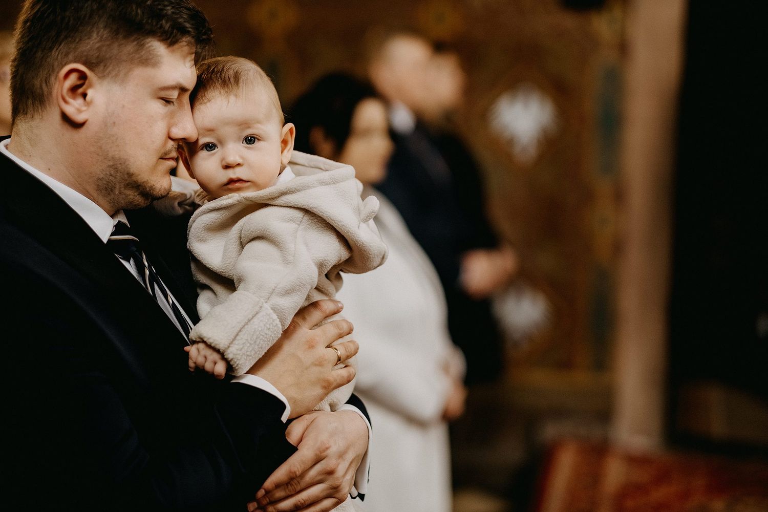 Tender moment as father holds sleeping infant close during solemn church baptism ceremony.