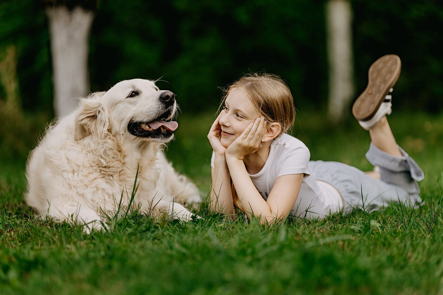 Young girl lying on grass face-to-face with happy golden retriever dog.