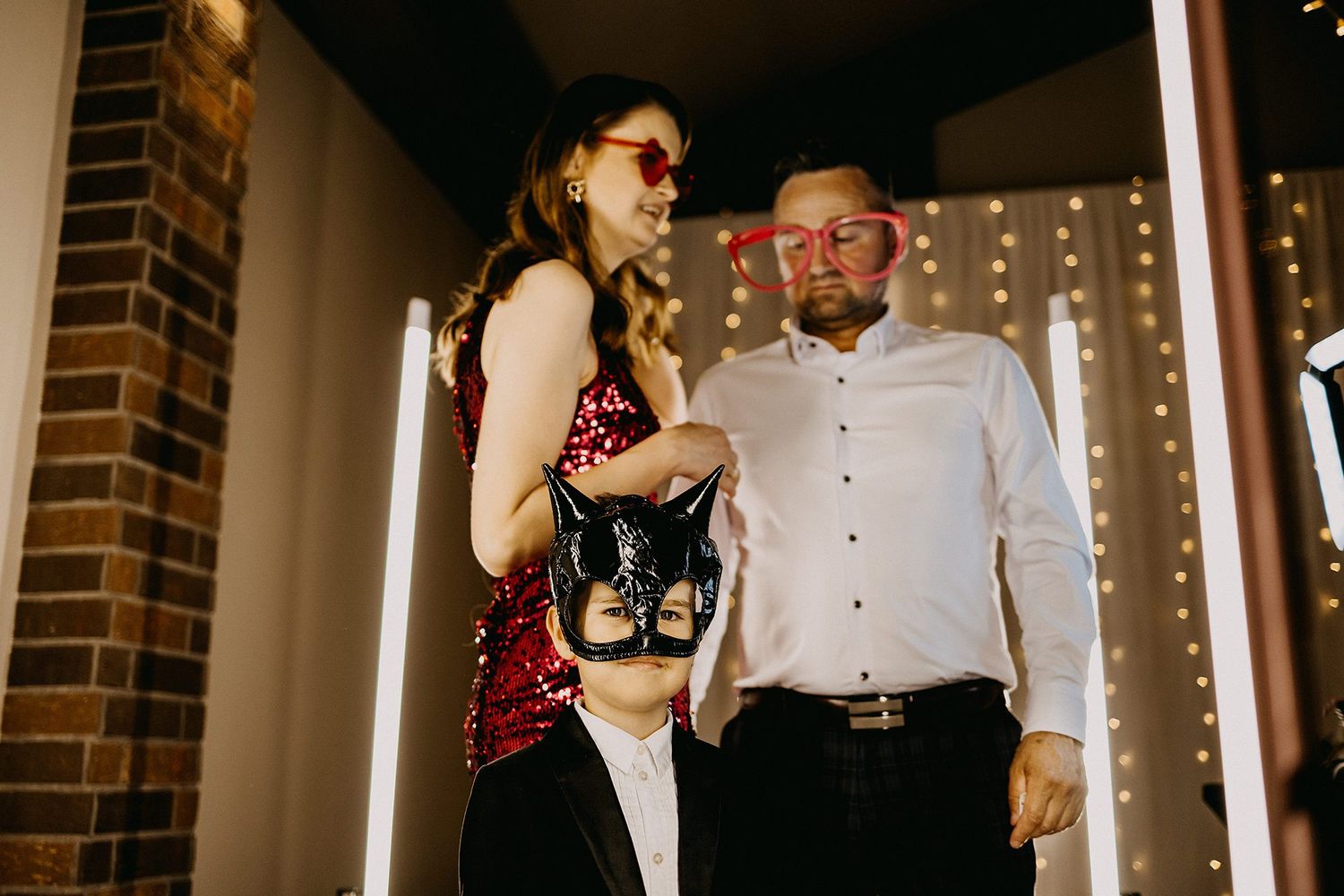 Family posing with fun photo booth props including oversized glasses and a masquerade mask.
