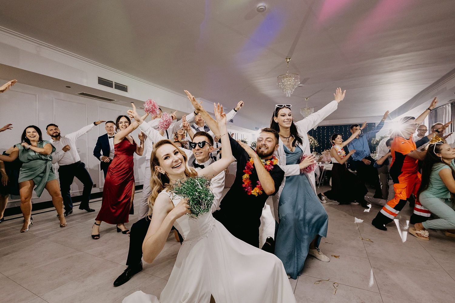 Joyful wedding reception dance floor with bride, groom, and guests celebrating with raised hands.