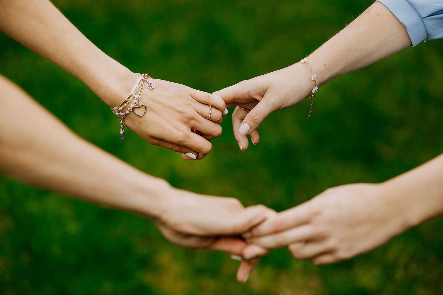 Close-up of hands touching with delicate bracelets over a green grass background.