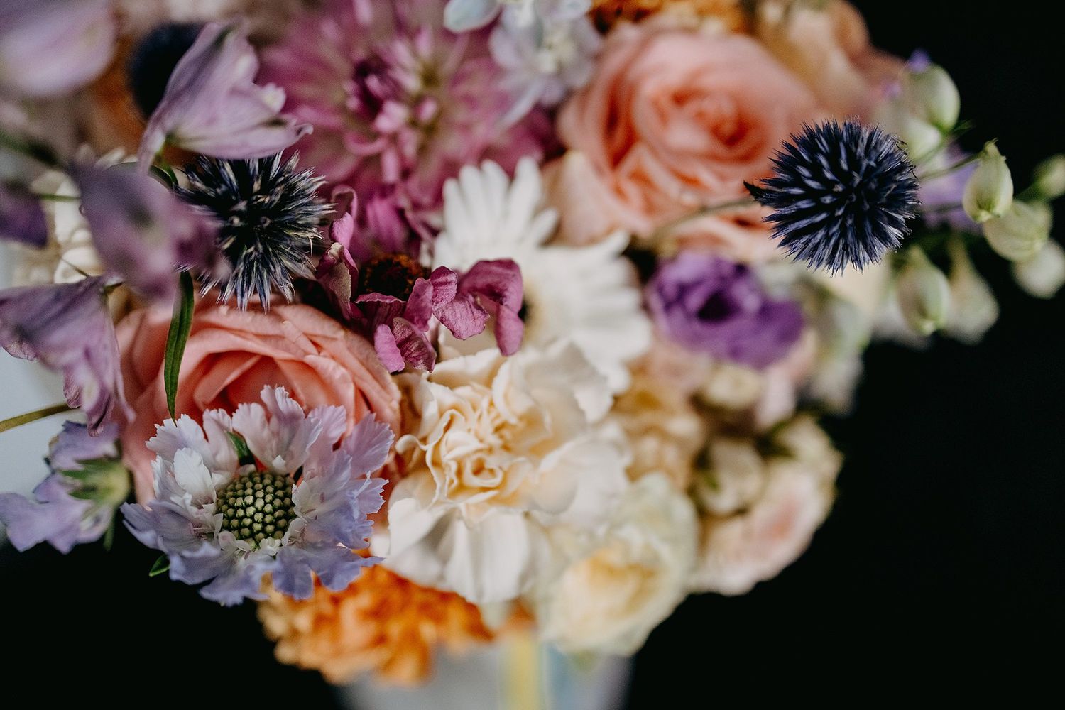 Close-up of colorful wedding bouquet featuring roses, purple thistle, and mixed blooms.