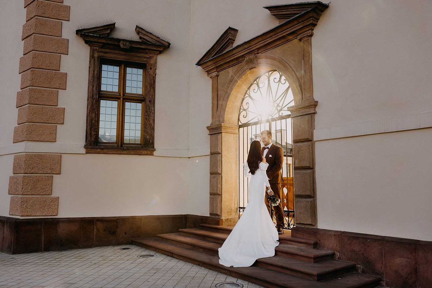 Bride and groom share a romantic kiss in a grand arched doorway of a historic European building.