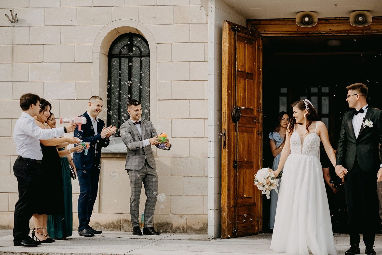 Bride and groom greeted by guests with confetti outside historic church doors.