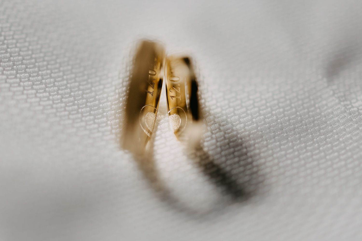 Close-up macro shot of two gold wedding rings resting on white fabric.
