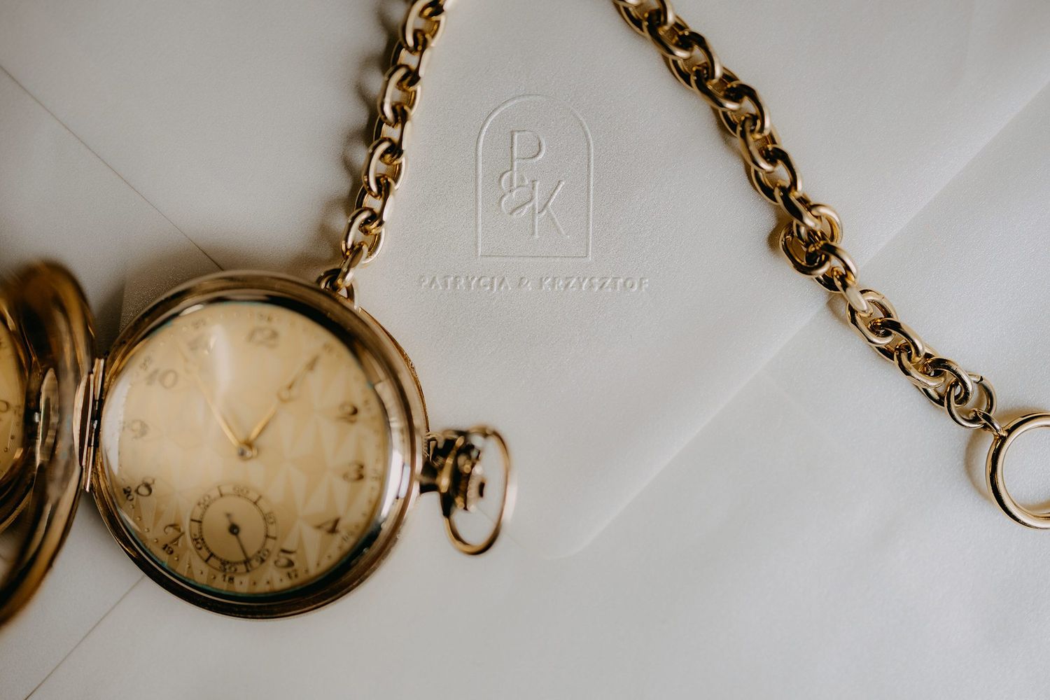 Antique gold pocket watch with chain on white envelope with embossed photographer logo.
