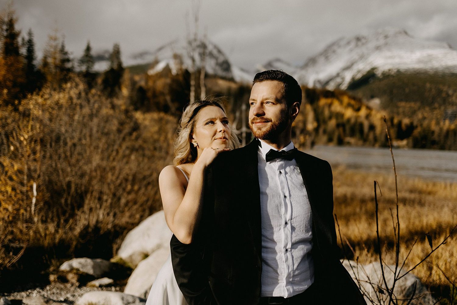 Bride tenderly touches grooms face as they sit together in an autumn mountain landscape.