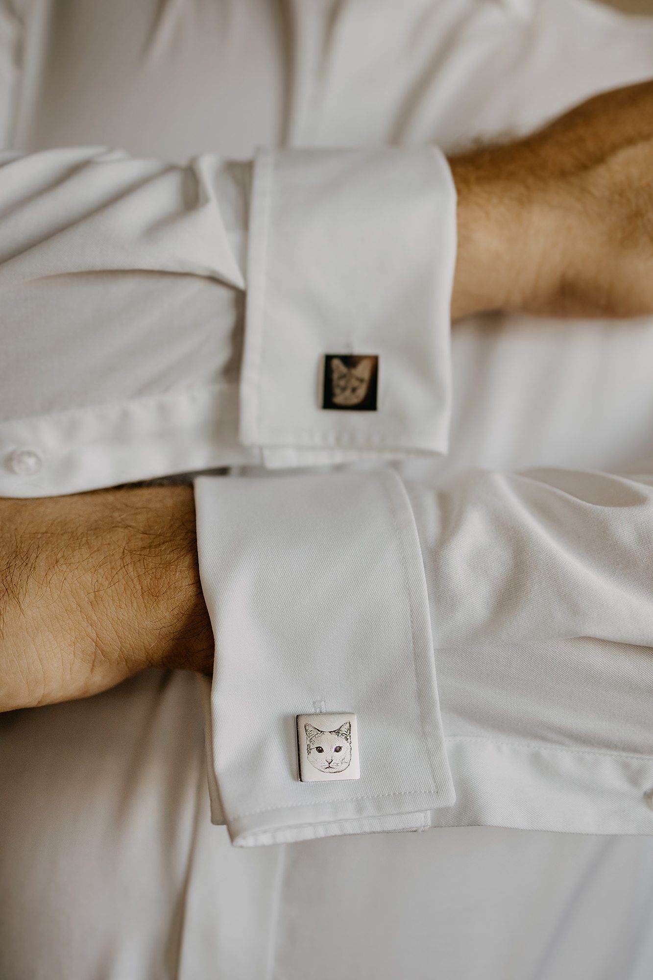 Close-up of groom's white shirt cufflinks featuring cat face designs on wedding day.